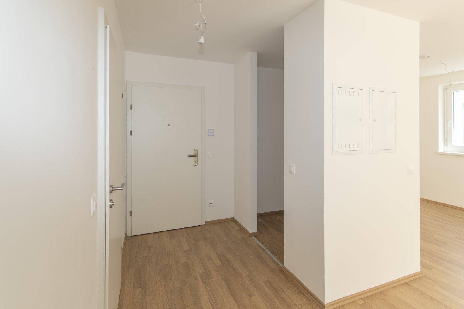 Heller Eingangsbereich mit Laminatboden und weißer Eingangstür in einem Neubau.