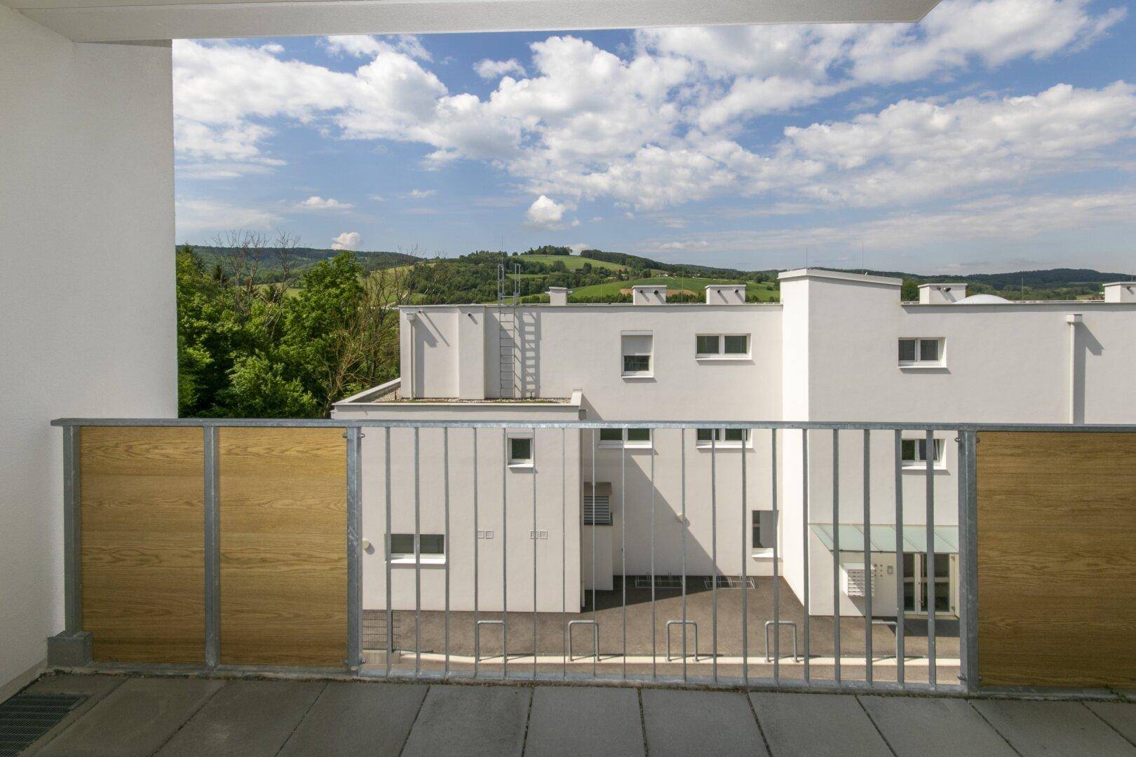 Heller Balkon mit Holzelementen am Geländer und weitem Blick über die Landschaft.