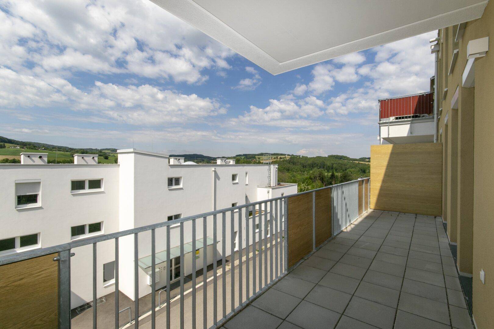 Langer Balkon mit Fliesenboden und Panoramablick auf die umliegende Natur und Wohngebäude.