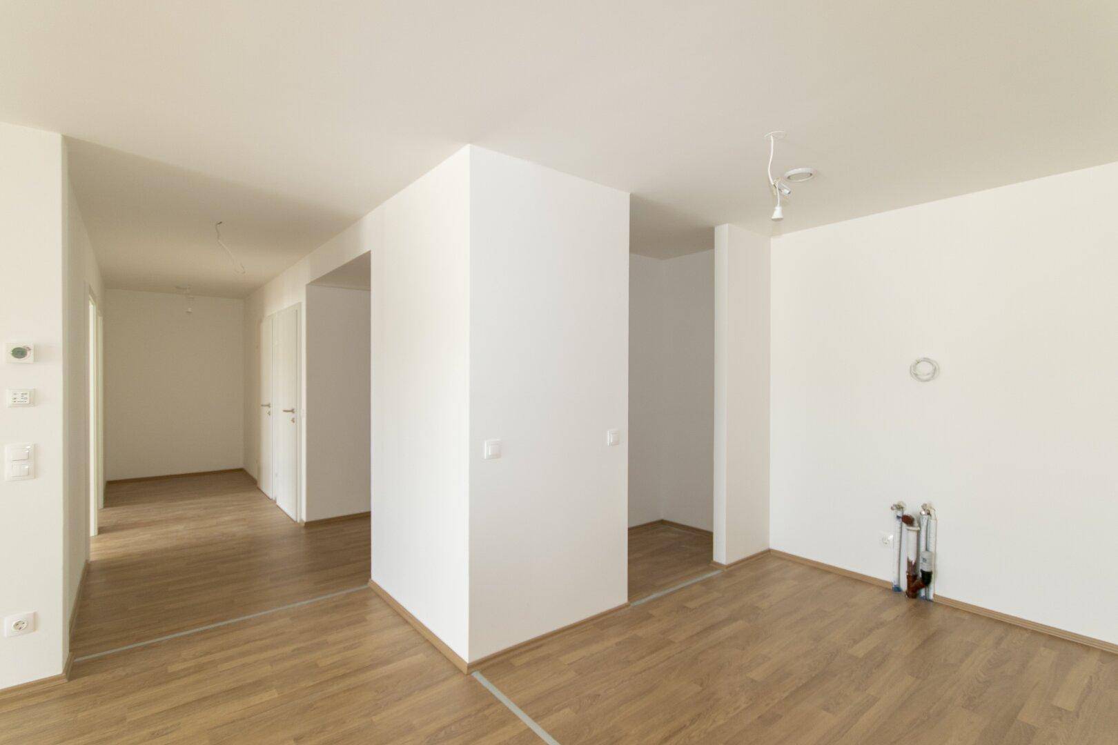 Leerer Raum mit Laminatboden und weißen Wänden, vorbereitet für die Installation einer Küche.