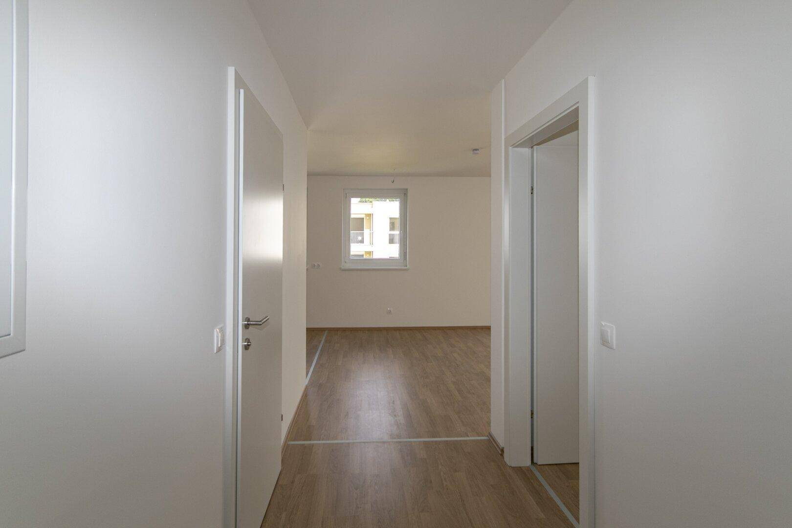 Langer Flur mit hellem Laminatboden und weißen Türen, der zu den verschiedenen Zimmern führt.