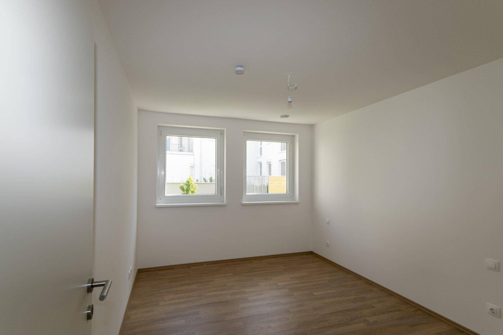 Helles Schlafzimmer mit zwei Fenstern und Laminatboden, bereit zur Einrichtung in einem Neubau.