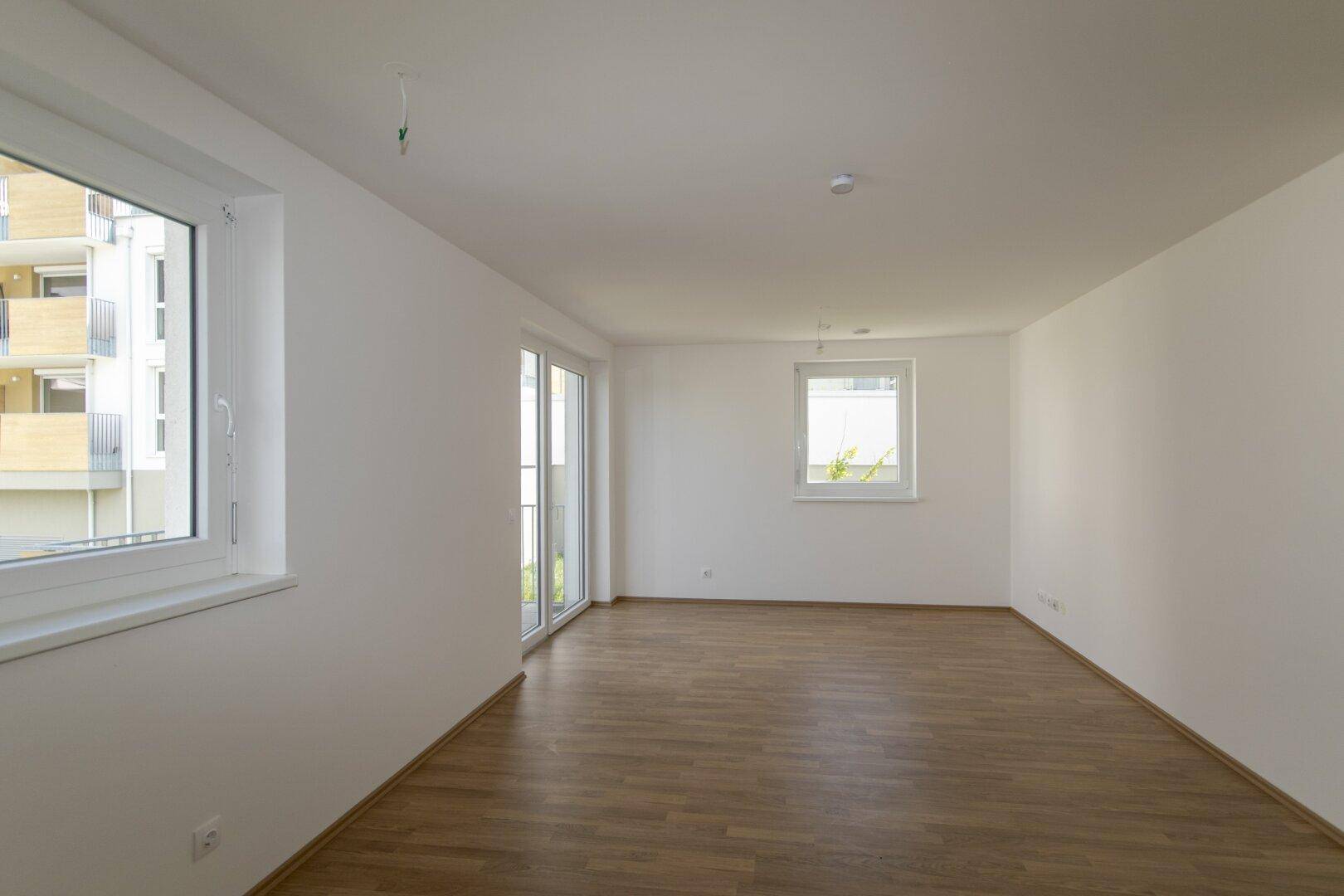 Geräumiges Zimmer mit hellem Laminatboden und mehreren Fenstern für viel Tageslicht und Ausblick.