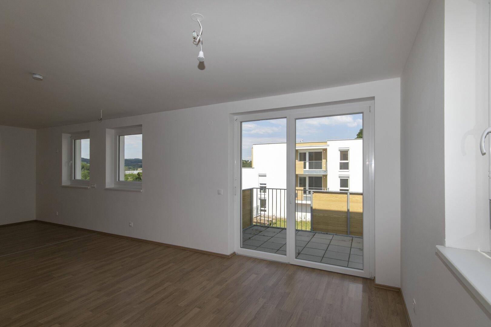Helles Wohnzimmer mit Laminatboden und direktem Zugang zu einem Balkon, bereit zur individuellen Gestaltung.
