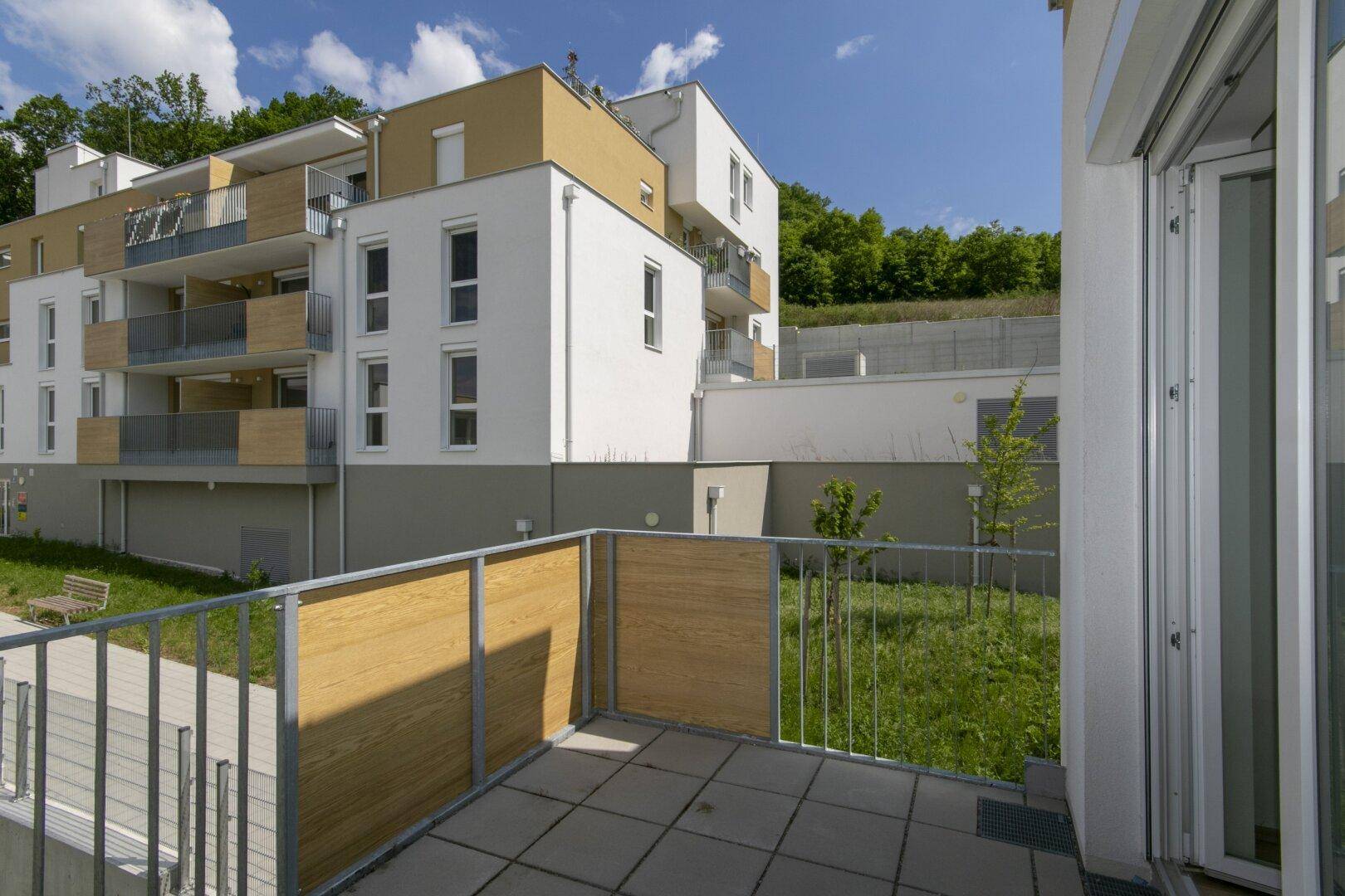 Balkon mit Fliesenboden und Blick auf die moderne Wohnanlage sowie eine kleine Grünfläche.