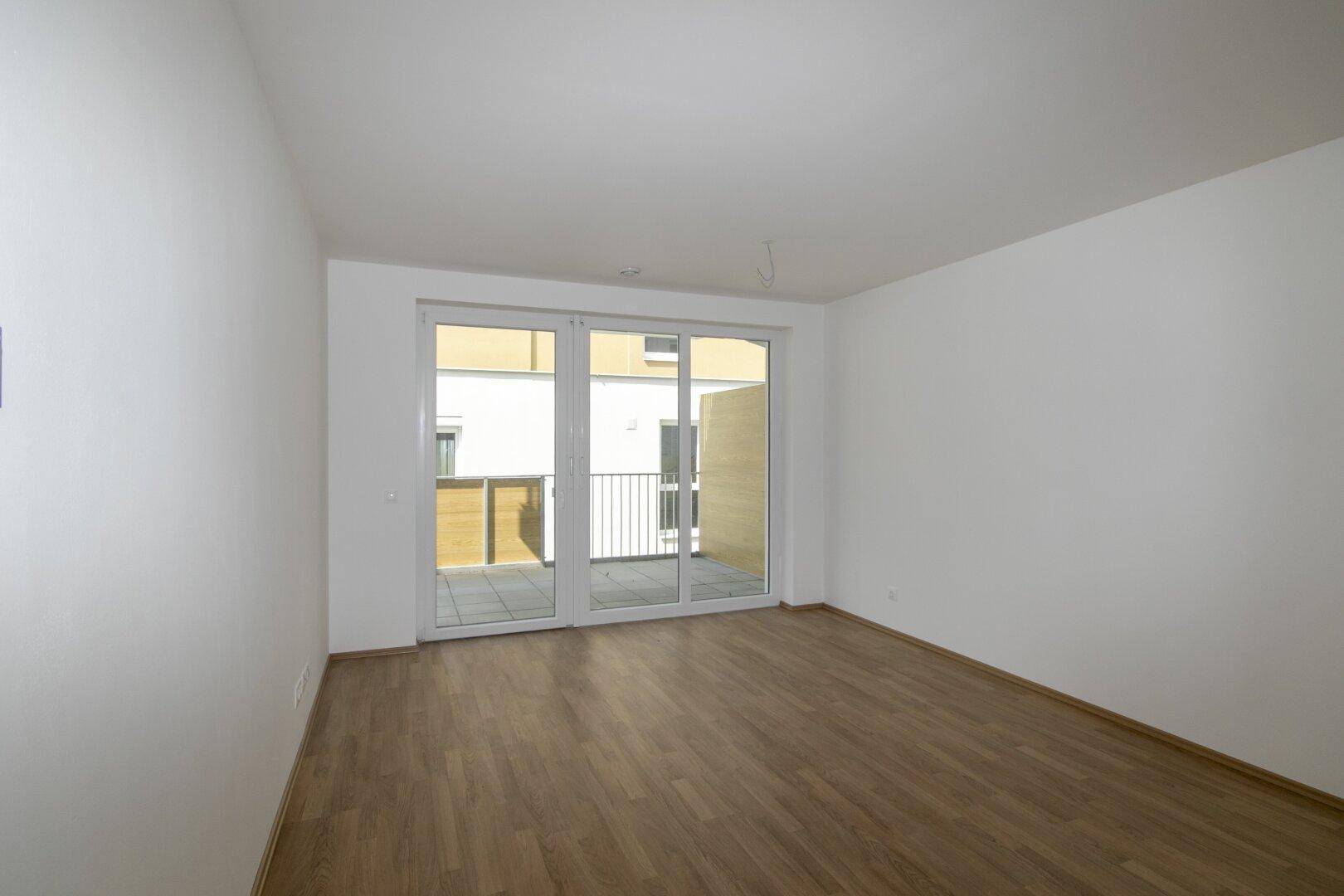 Heller, leerer Raum mit Laminatboden und Zugang zu einer Terrasse durch große Glastüren.