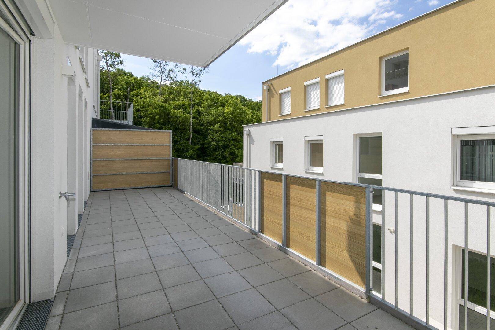 Breite Terrasse mit Fliesenboden und Holzelementen, umgeben von modernen Gebäuden und Bäumen.