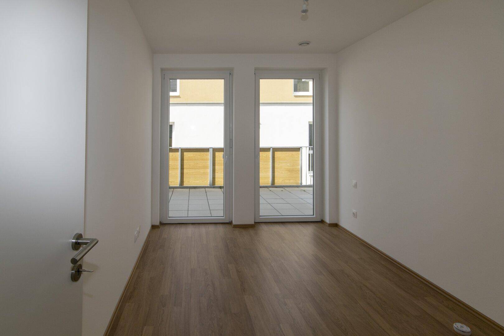 Schlafzimmer mit Holzboden und direktem Zugang zum Balkon, bietet viel natürliches Licht.