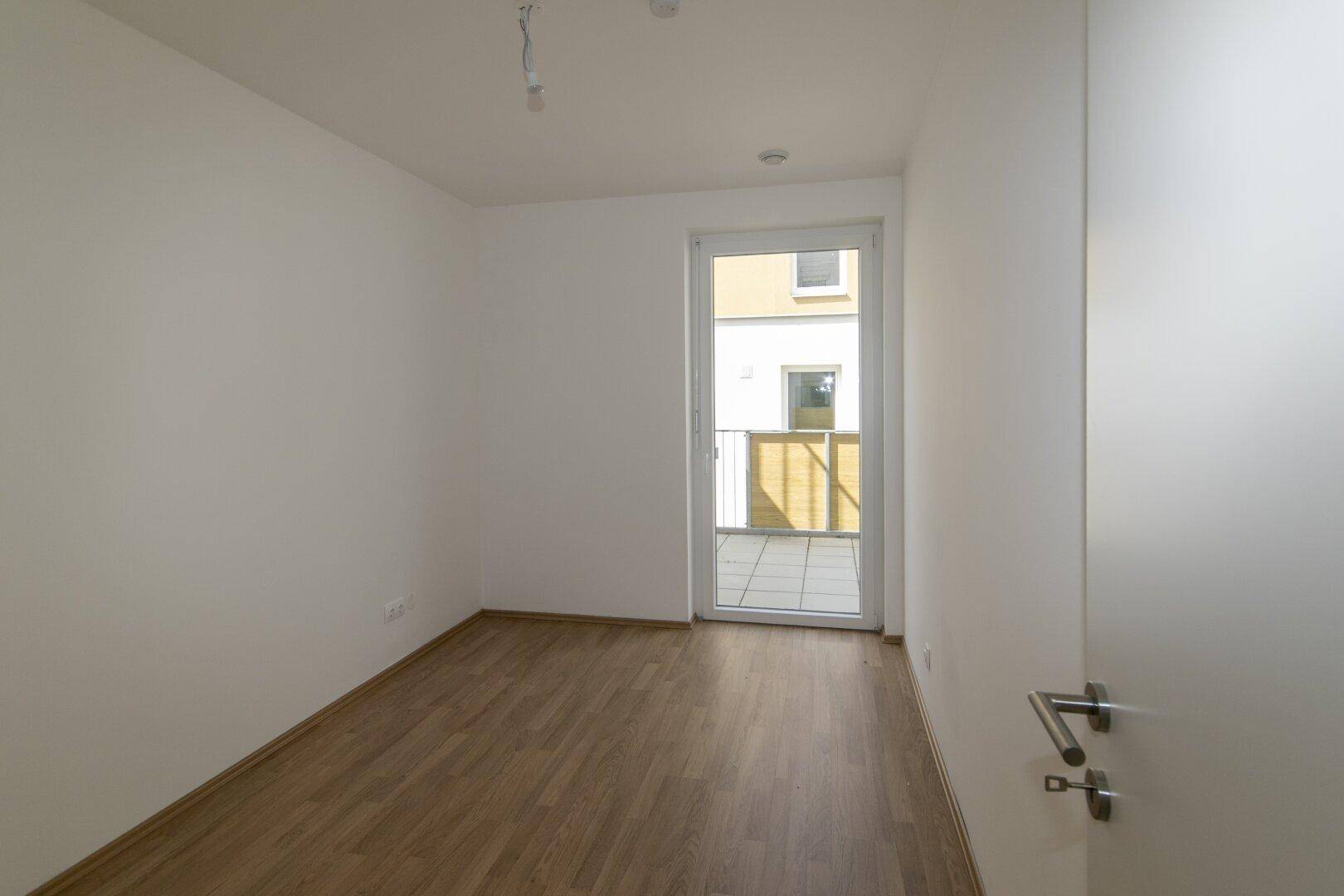 Helles Schlafzimmer mit Holzboden und Balkontür, ideal für Ruhe und Entspannung.