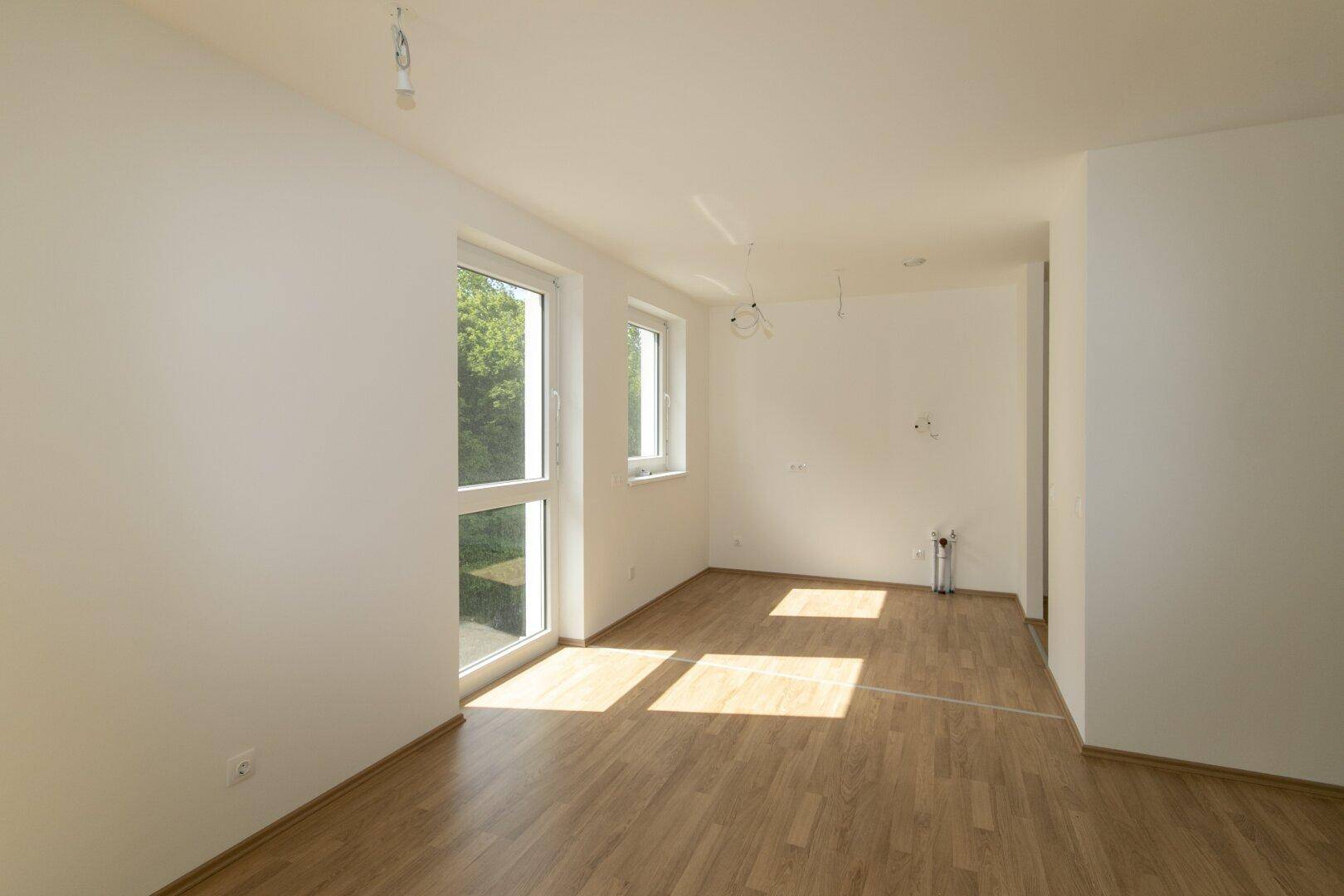 Heller Raum mit Laminatboden und weißen Wänden, vorbereitet für die Installation einer Küche oder eines Wohnbereichs.