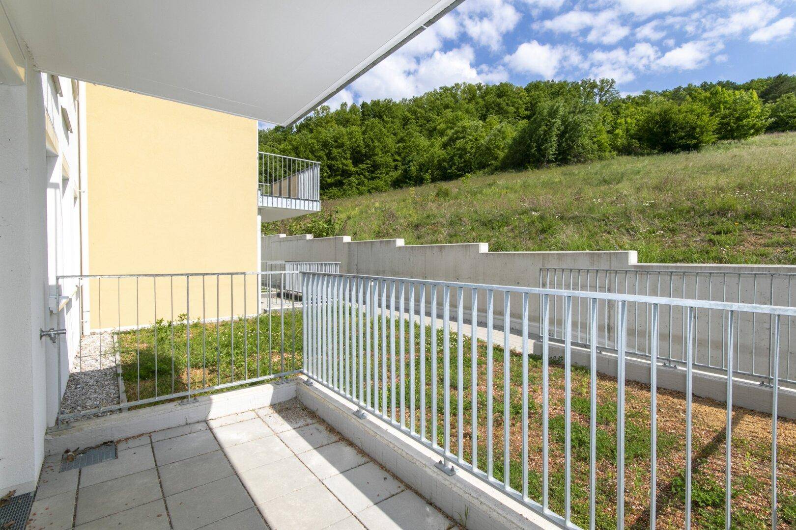 Geräumige Terrasse mit Blick auf die umliegende Natur und die gelbe Gebäudefassade.