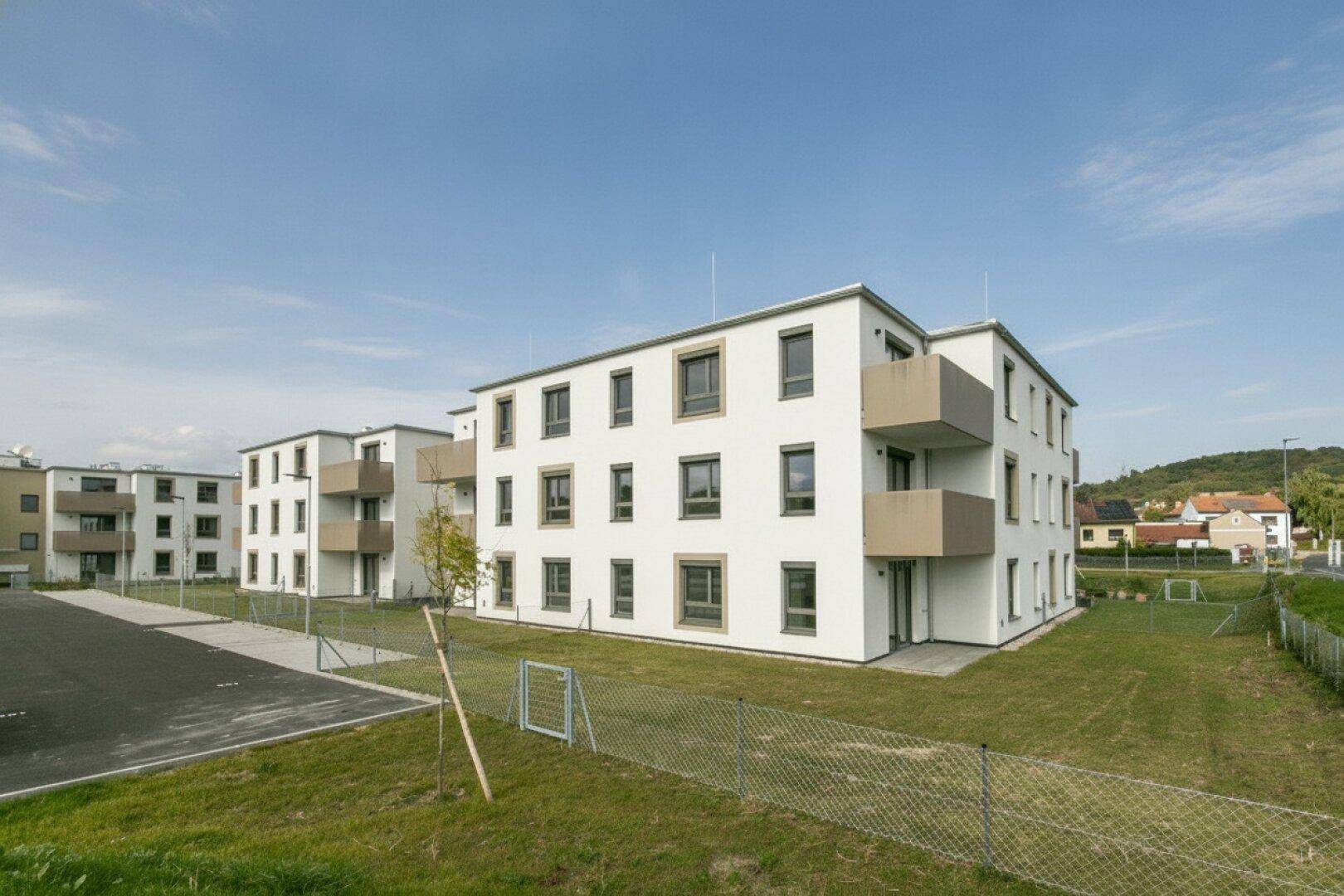 Moderne Wohngebäude mit Balkonen und neu angelegten Parkplätzen, eingebettet in eine hügelige Landschaft.