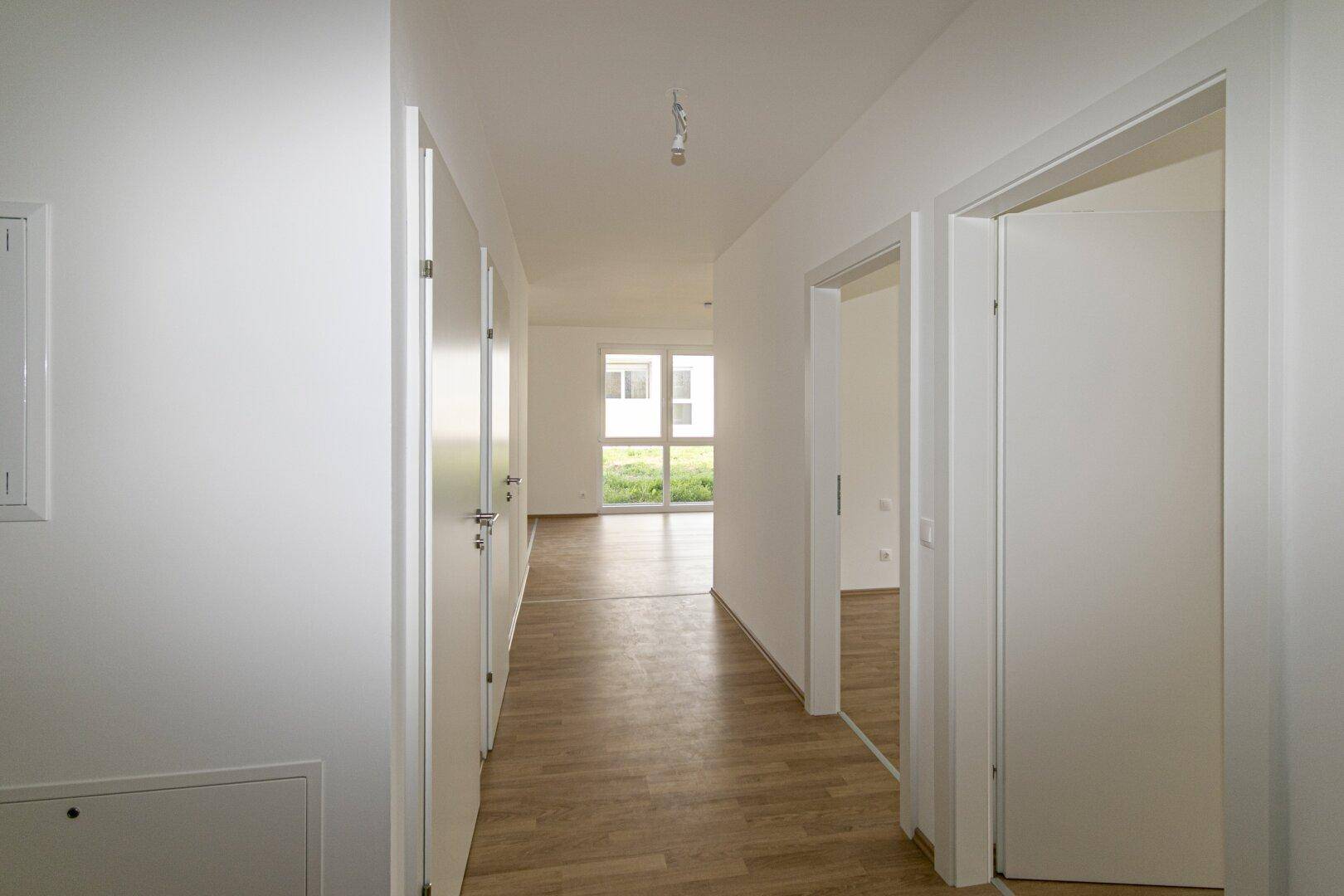 Langer, heller Flur mit Holzboden und weißen Türen, der zu weiteren Räumen führt.