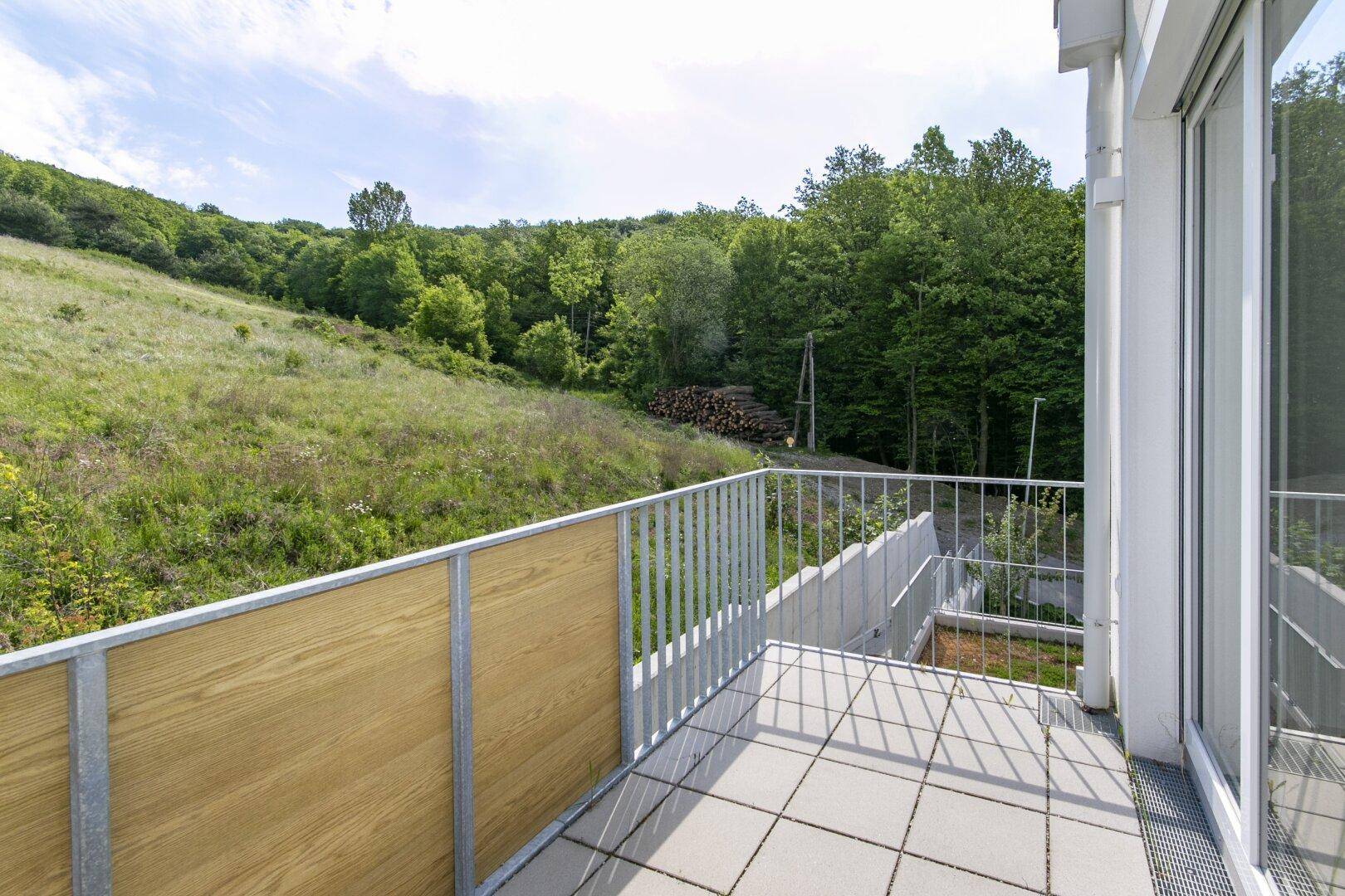 Balkon mit Fliesenboden und weitem Blick über die grüne Landschaft und gestapeltes Holz.