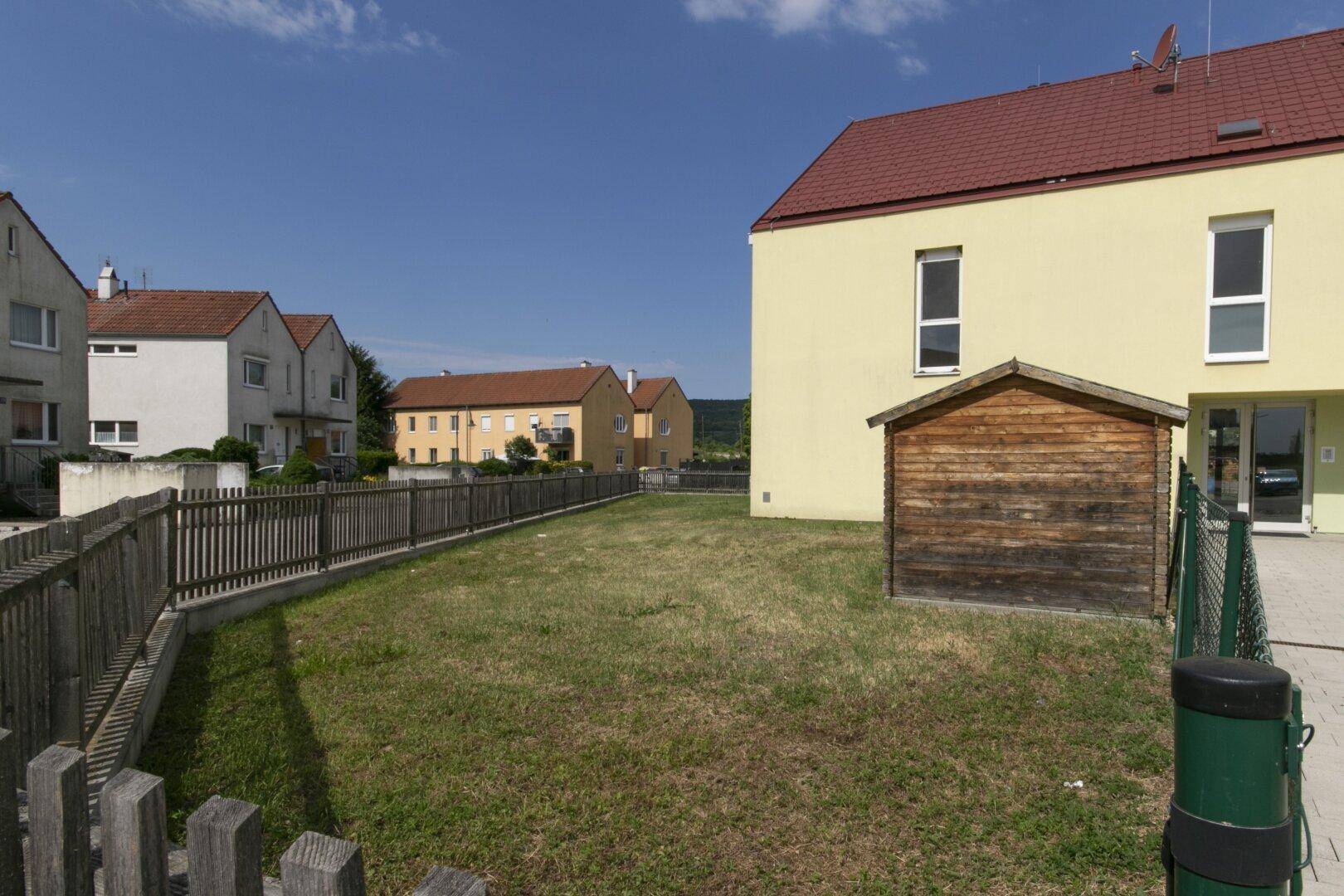 Rückansicht des Gebäudes mit einem Holzschuppen und einem Zaun unter klarem blauem Himmel.