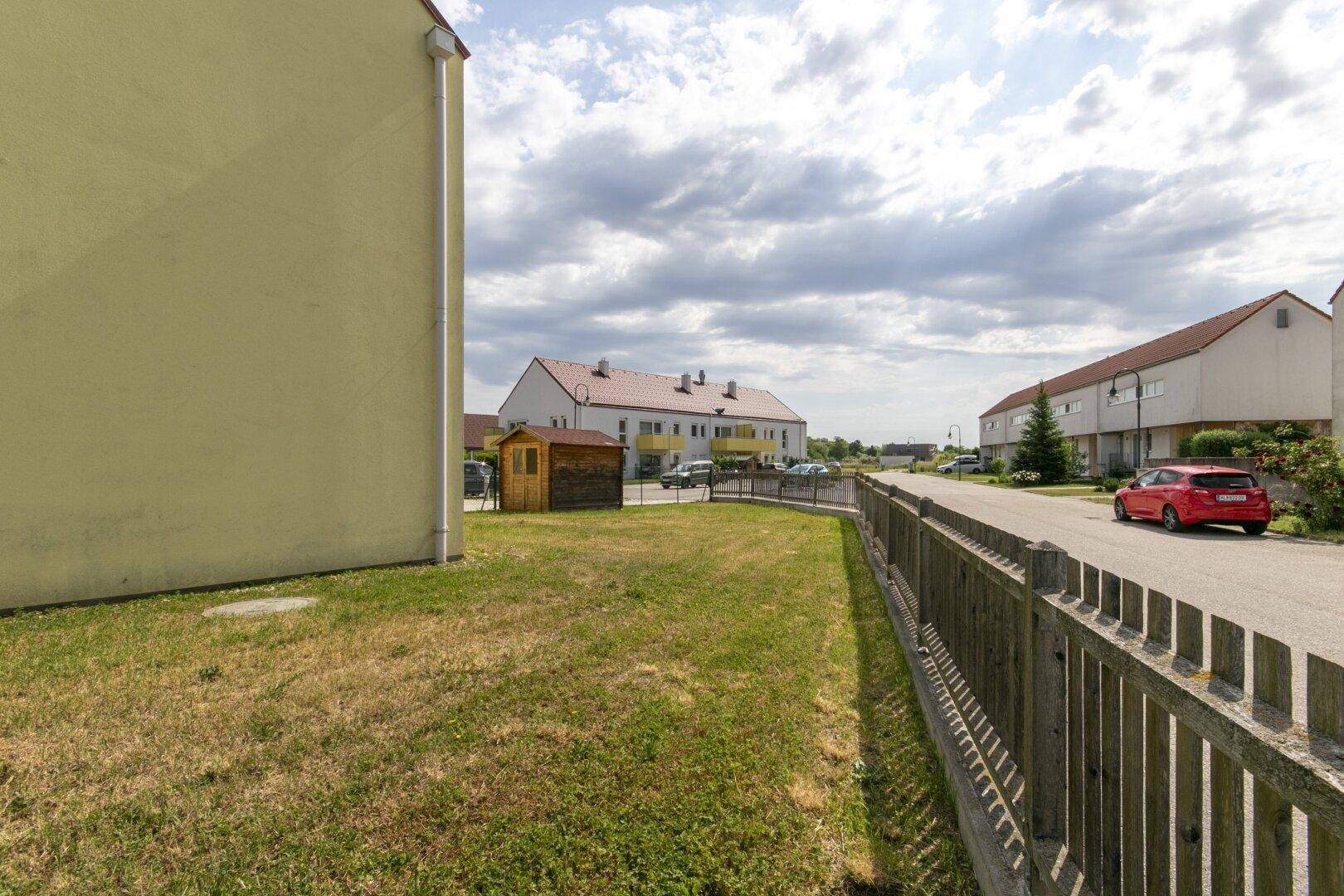 Seitenansicht des Gebäudes mit einem kleinen Holzschuppen und einem Zaun entlang der Straße.