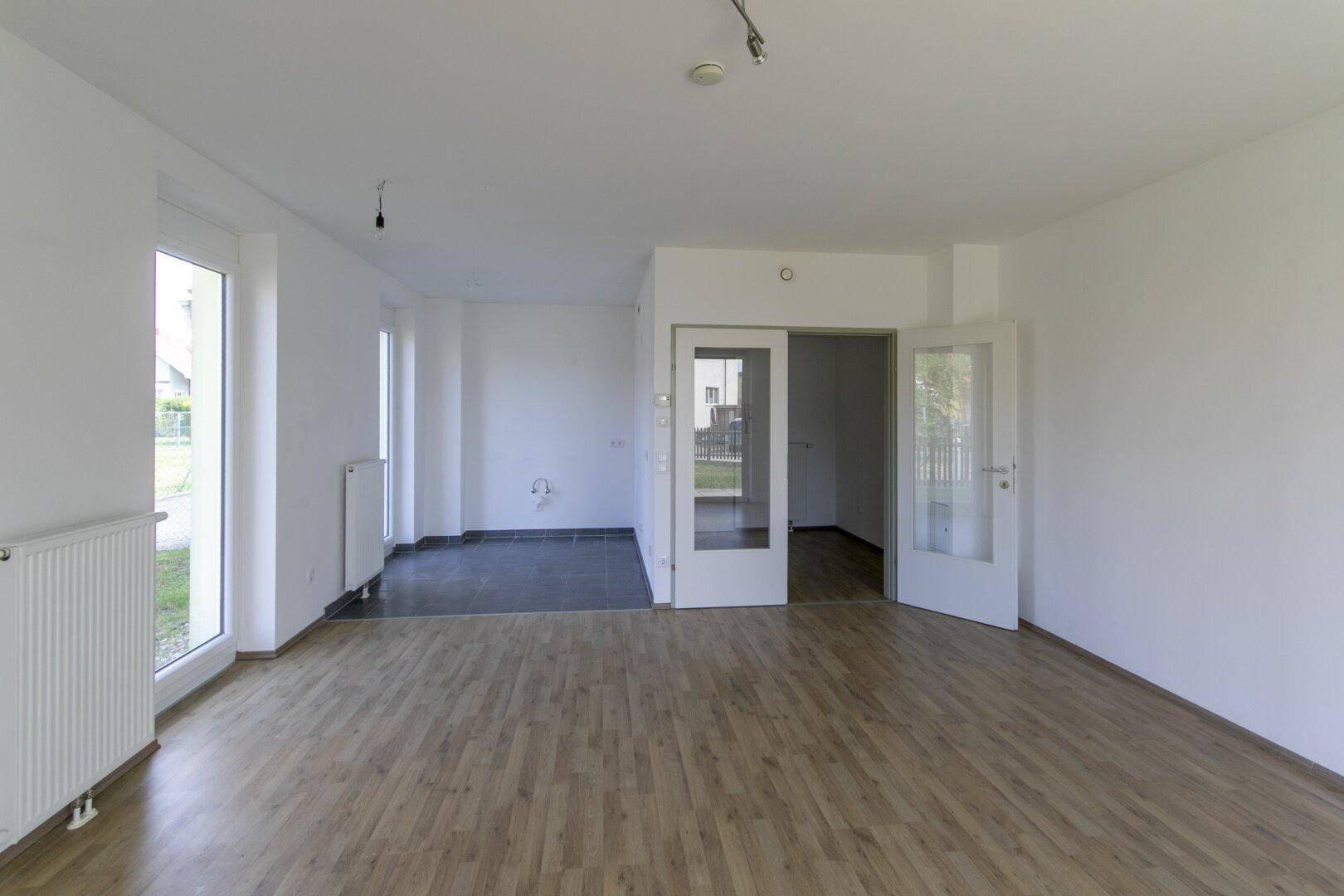 Geräumiger, leerer Raum mit Laminatboden, weißen Wänden und Übergang zu einem gefliesten Bereich.