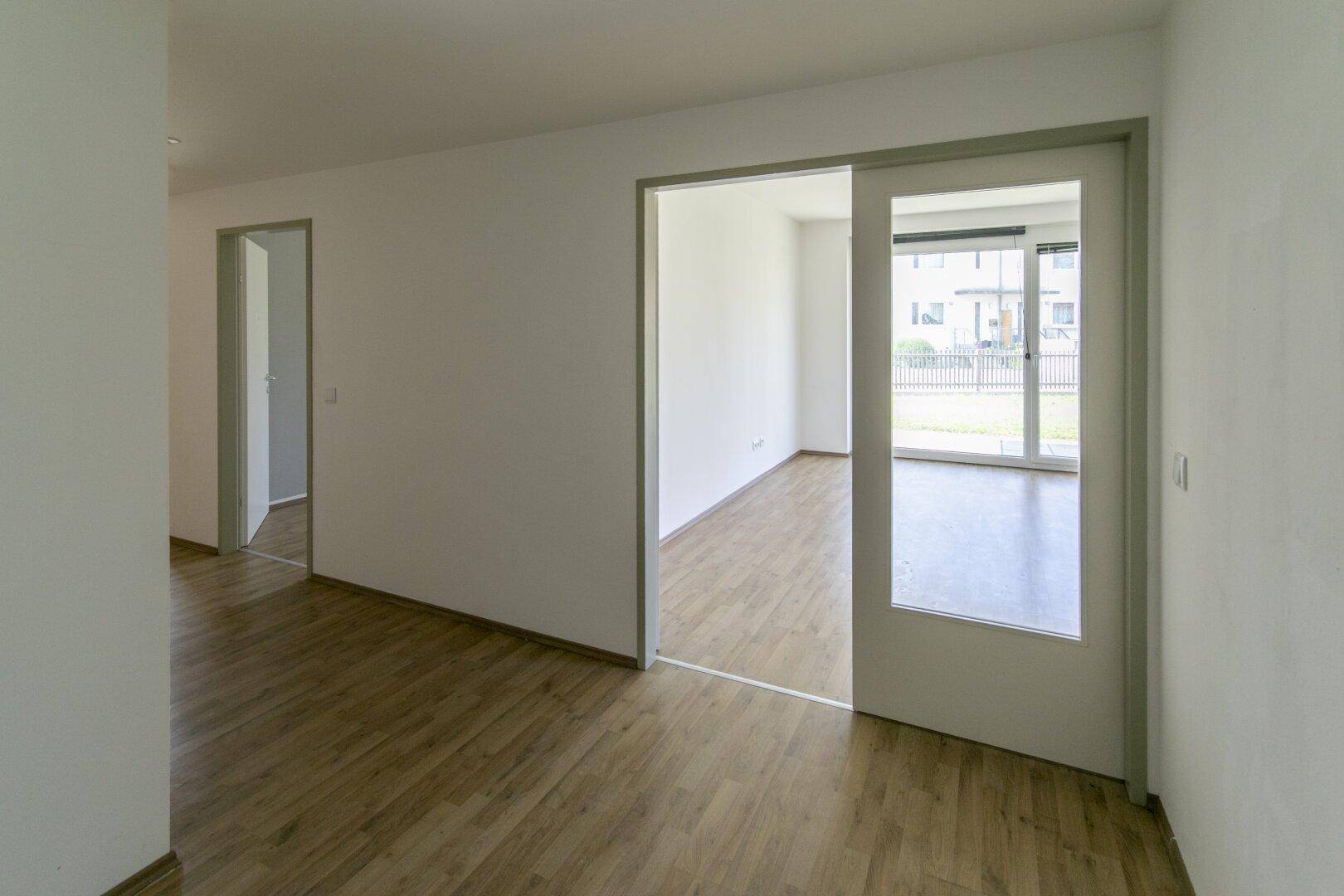 Heller Flur mit Laminatboden und weißen Wänden, der zu einem weiteren Zimmer führt.