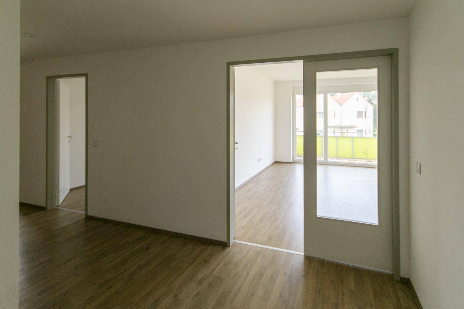 Heller Flur mit Laminatboden und Schiebetür, die zu einem weiteren Wohnbereich führt.