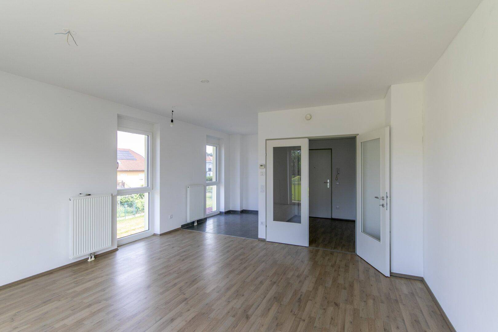 Geräumiger Wohnbereich mit Laminatboden, hellen Wänden und Übergang zu einem gefliesten Bereich.