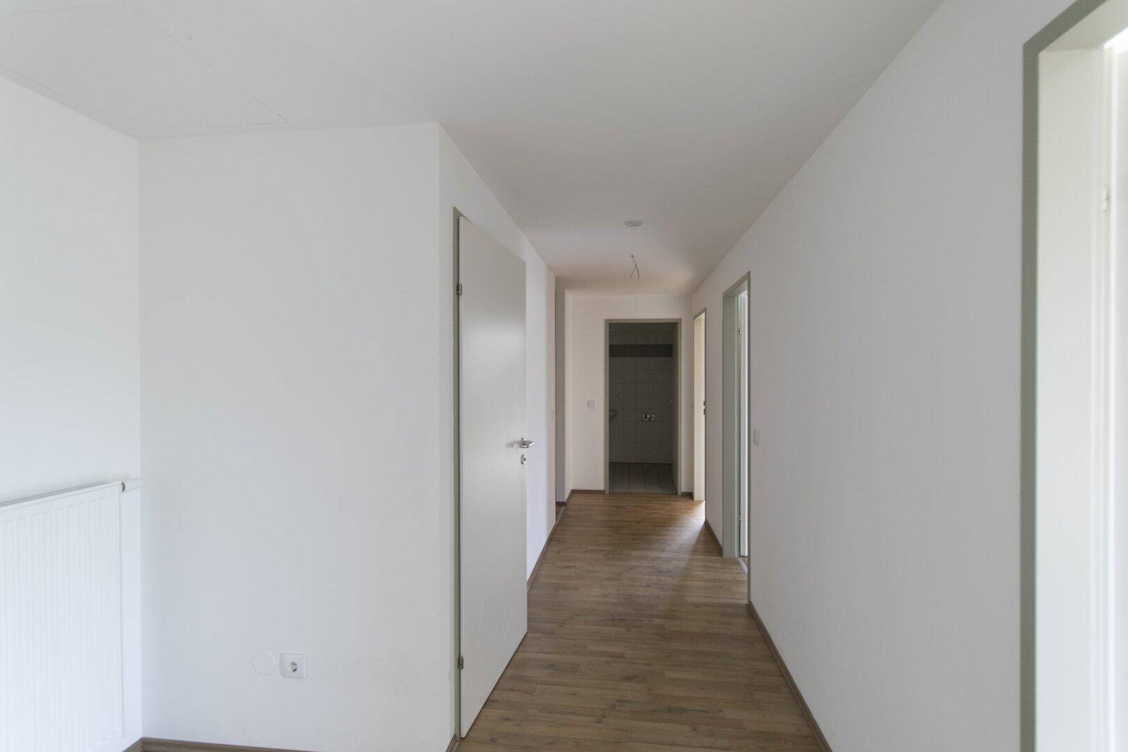 Langer, heller Flur mit Laminatboden und mehreren Türen zu den angrenzenden Zimmern.