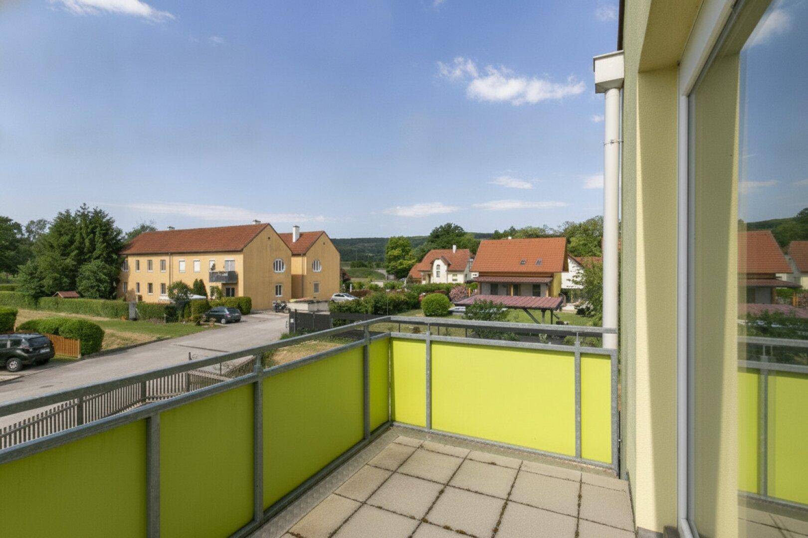 Sonniger Balkon mit Blick auf die Nachbarschaft und die hügelige Landschaft im Hintergrund.