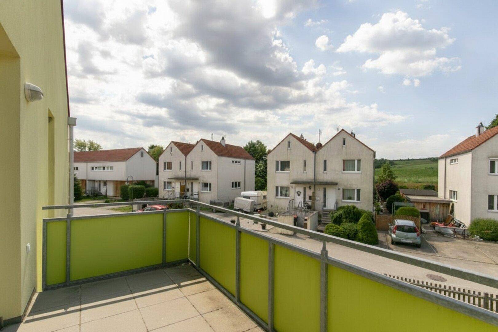 Balkon mit grüner Verkleidung und Ausblick auf eine Wohnsiedlung mit angrenzender Natur.