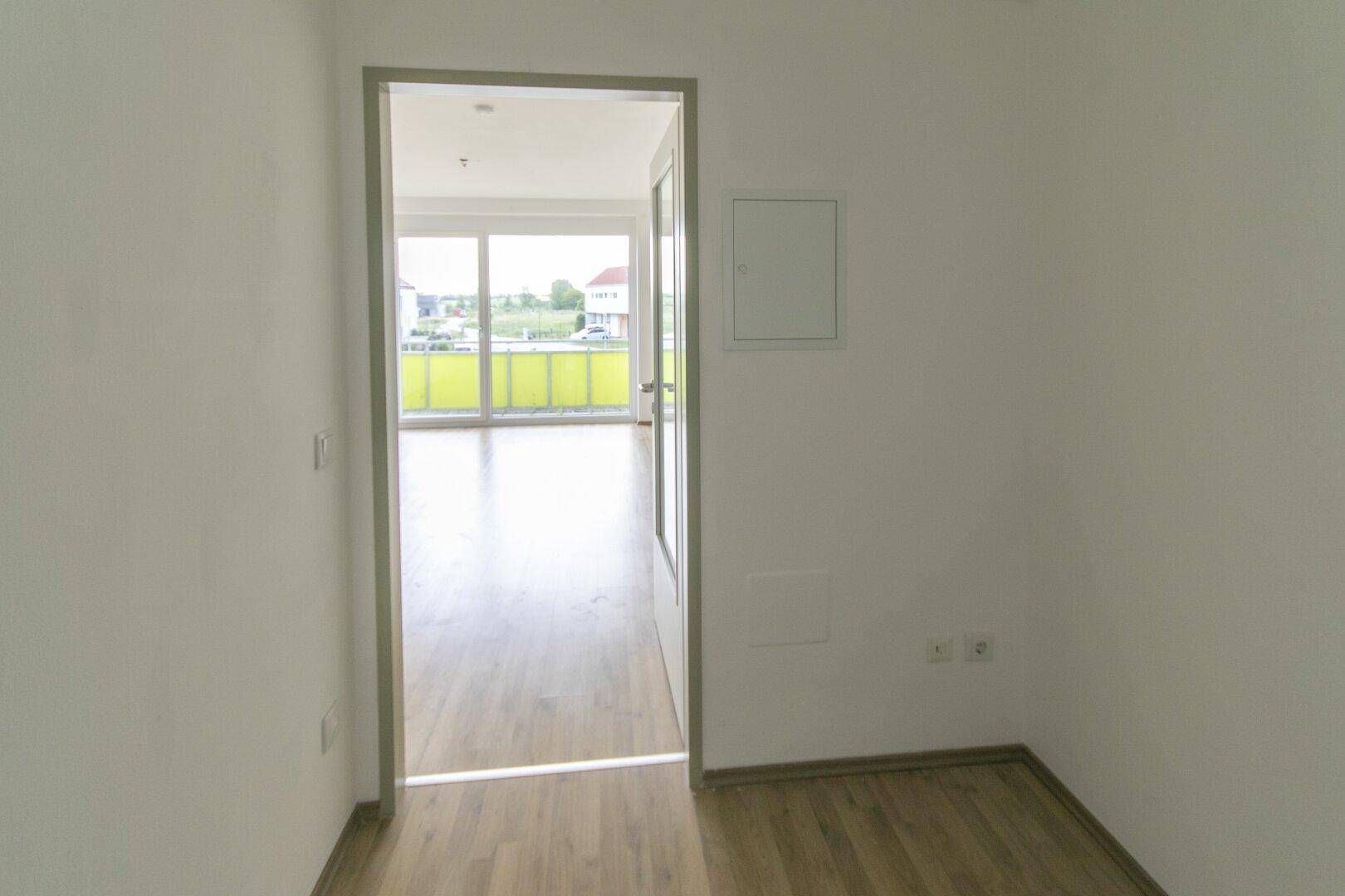 Flur mit Laminatboden und Blick in einen hellen Raum mit Zugang zum Balkon.