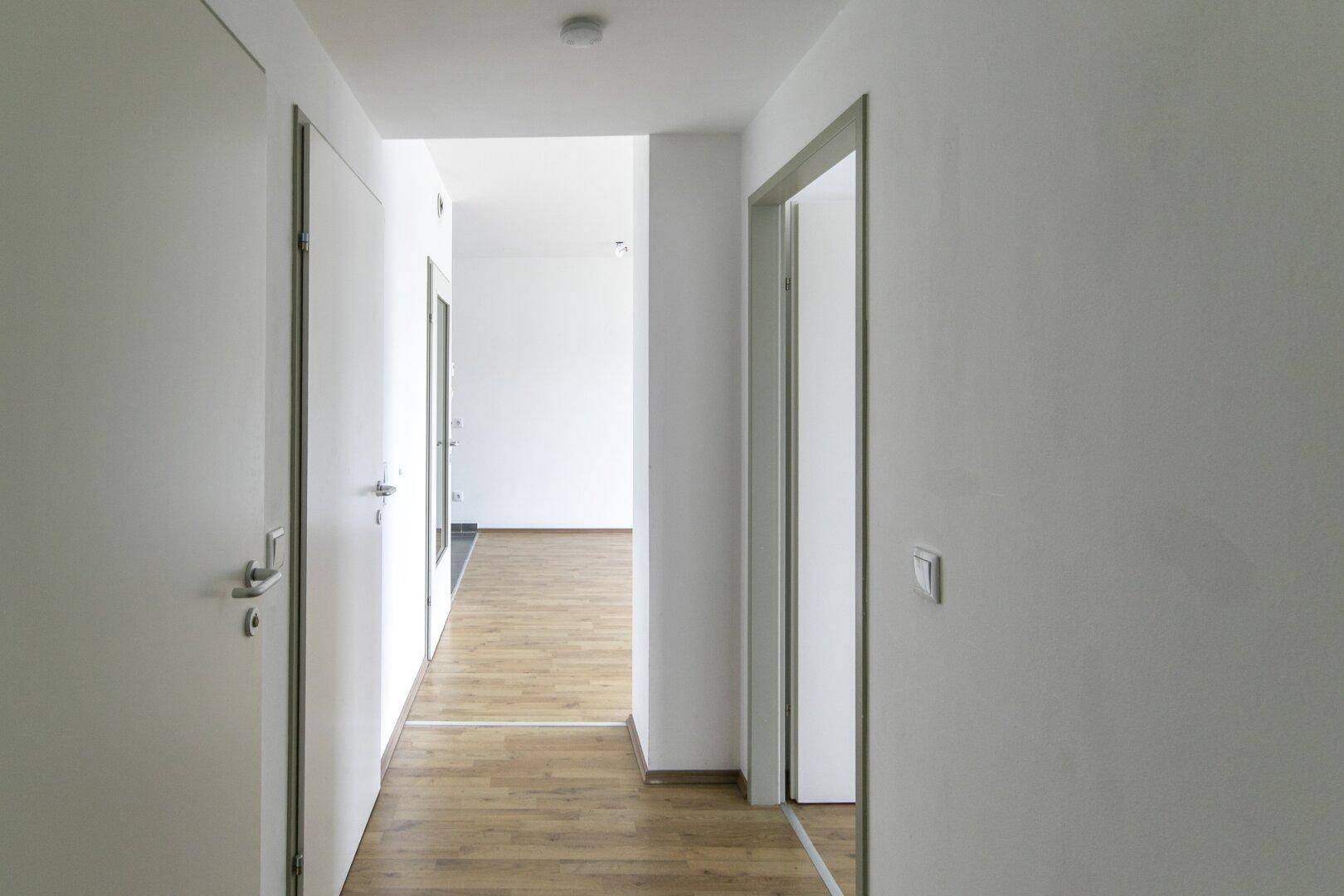 Geräumiger Flur mit hellem Laminatboden, der zu verschiedenen Zimmern führt.