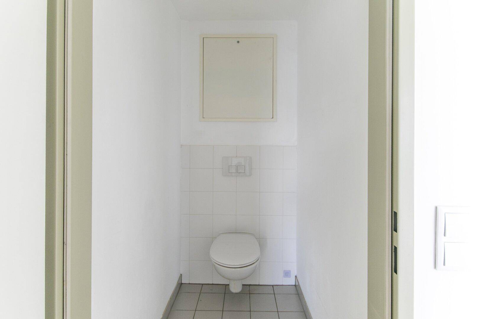 Schlichtes Gäste-WC mit Wand-WC und weißen Fliesen, funktional und sauber.