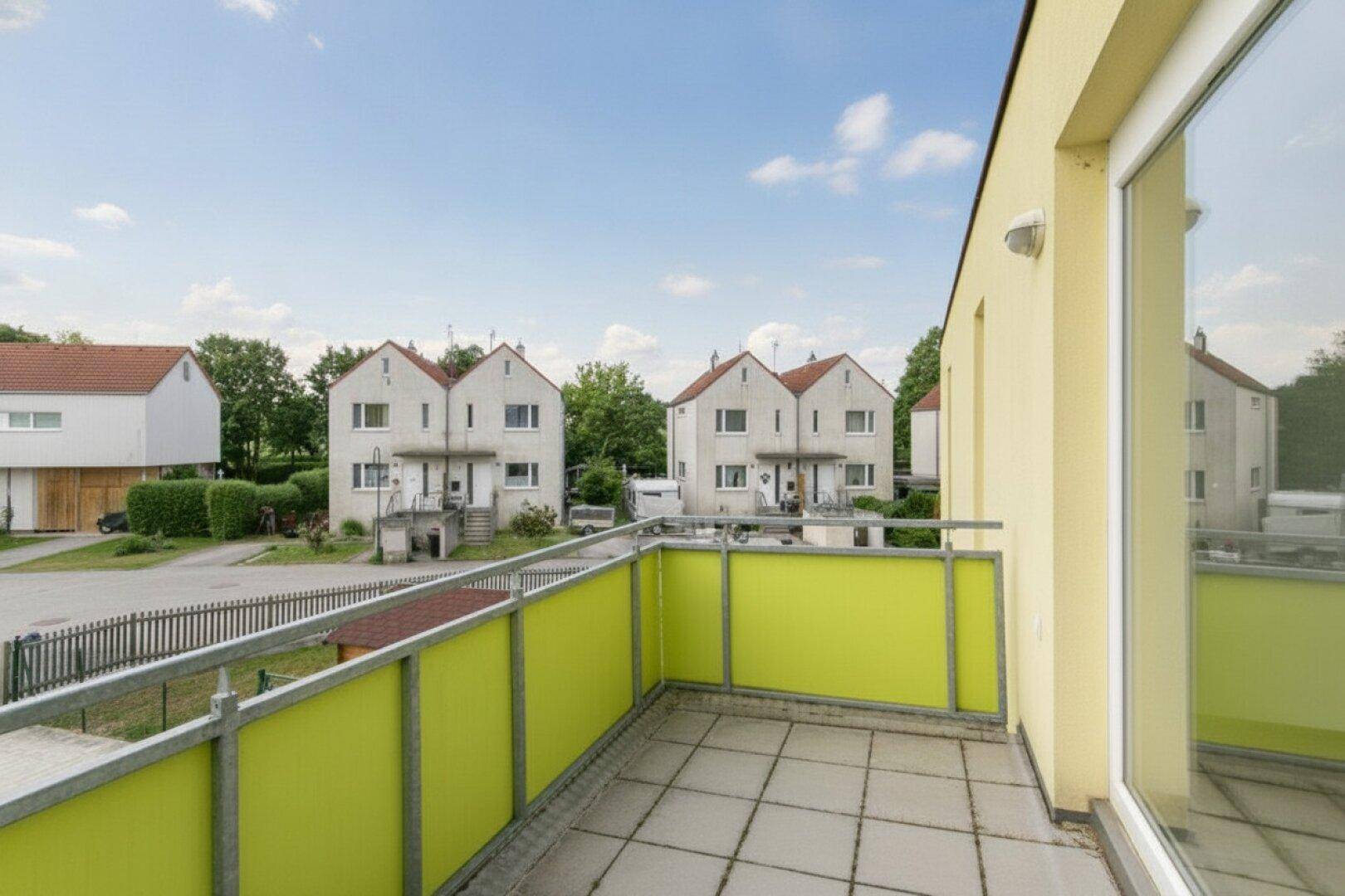 Heller Balkon mit grünen Paneelen und Ausblick auf die gegenüberliegenden Wohnhäuser.