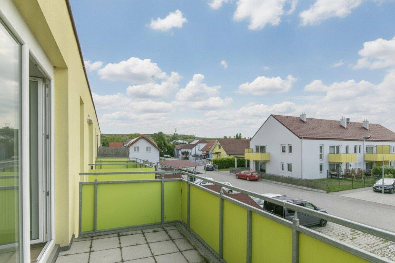 Balkon mit heller Brüstung und weitem Blick über die Nachbarschaft unter blauem Himmel.