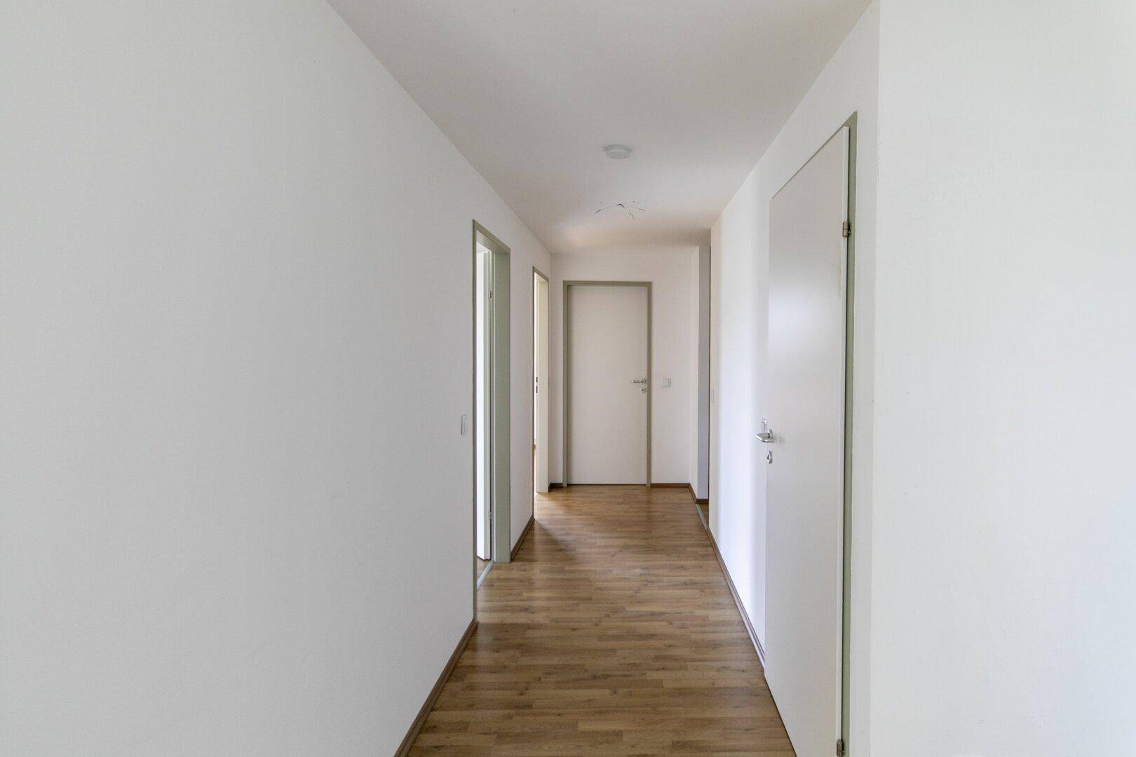 Langer, heller Flur mit Laminatboden und mehreren Türen zu den angrenzenden Zimmern.