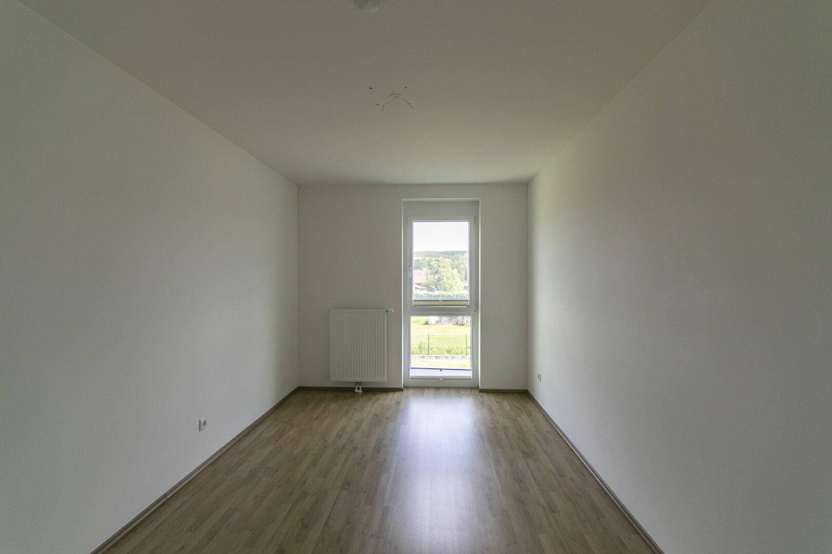 Helles Zimmer mit Laminatboden und großem Fenster, ideal als Schlaf- oder Arbeitszimmer.