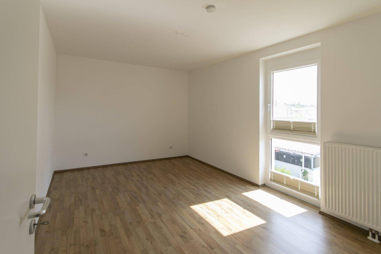 Sonniger Raum mit Laminatboden und großem Fenster, das viel Tageslicht hereinlässt.
