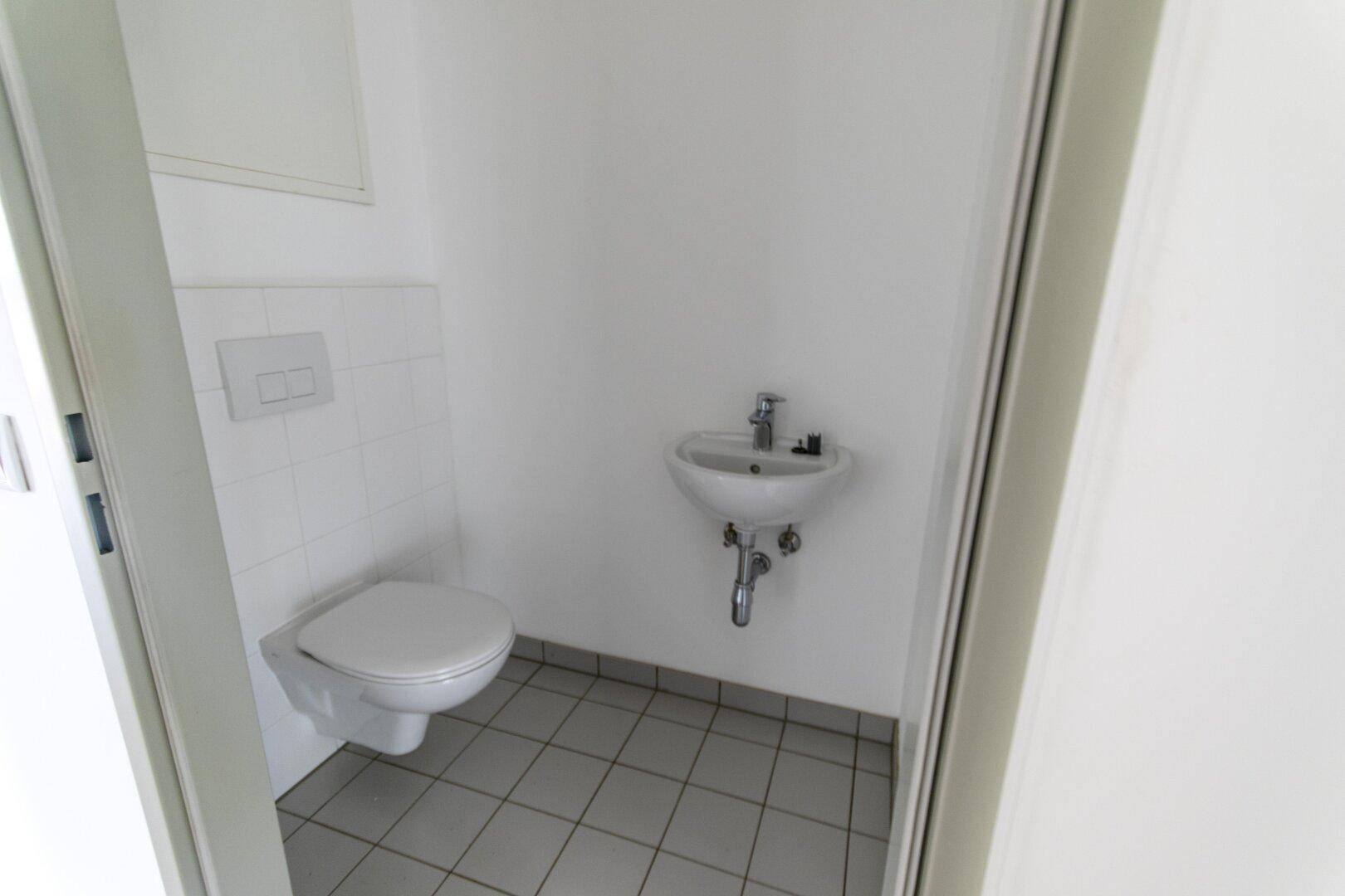 Kleines Gäste-WC mit wandhängendem WC, Waschbecken und hellen Fliesen.