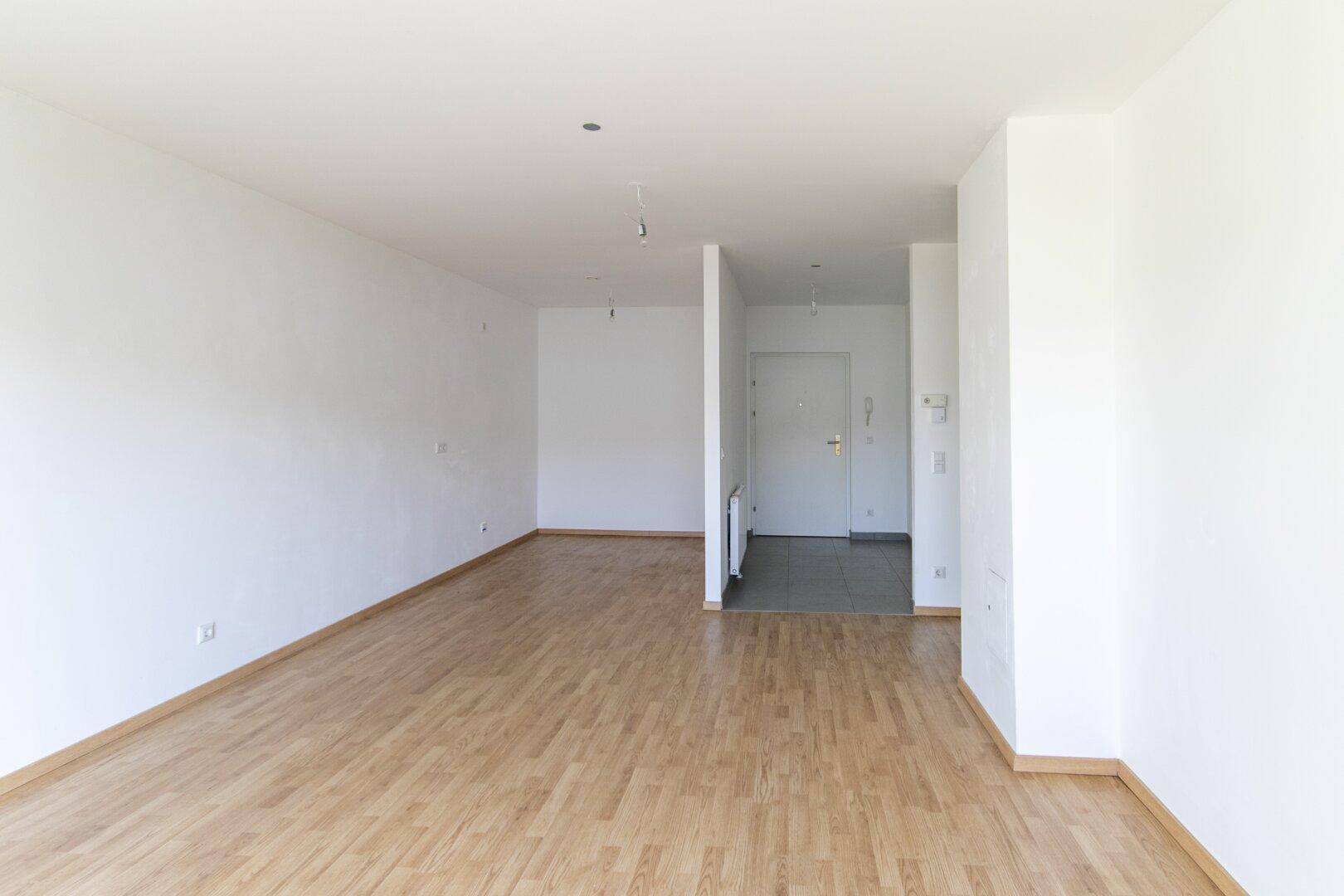 Geräumiger, heller Wohnbereich mit Laminatboden und weiß gestrichenen Wänden.