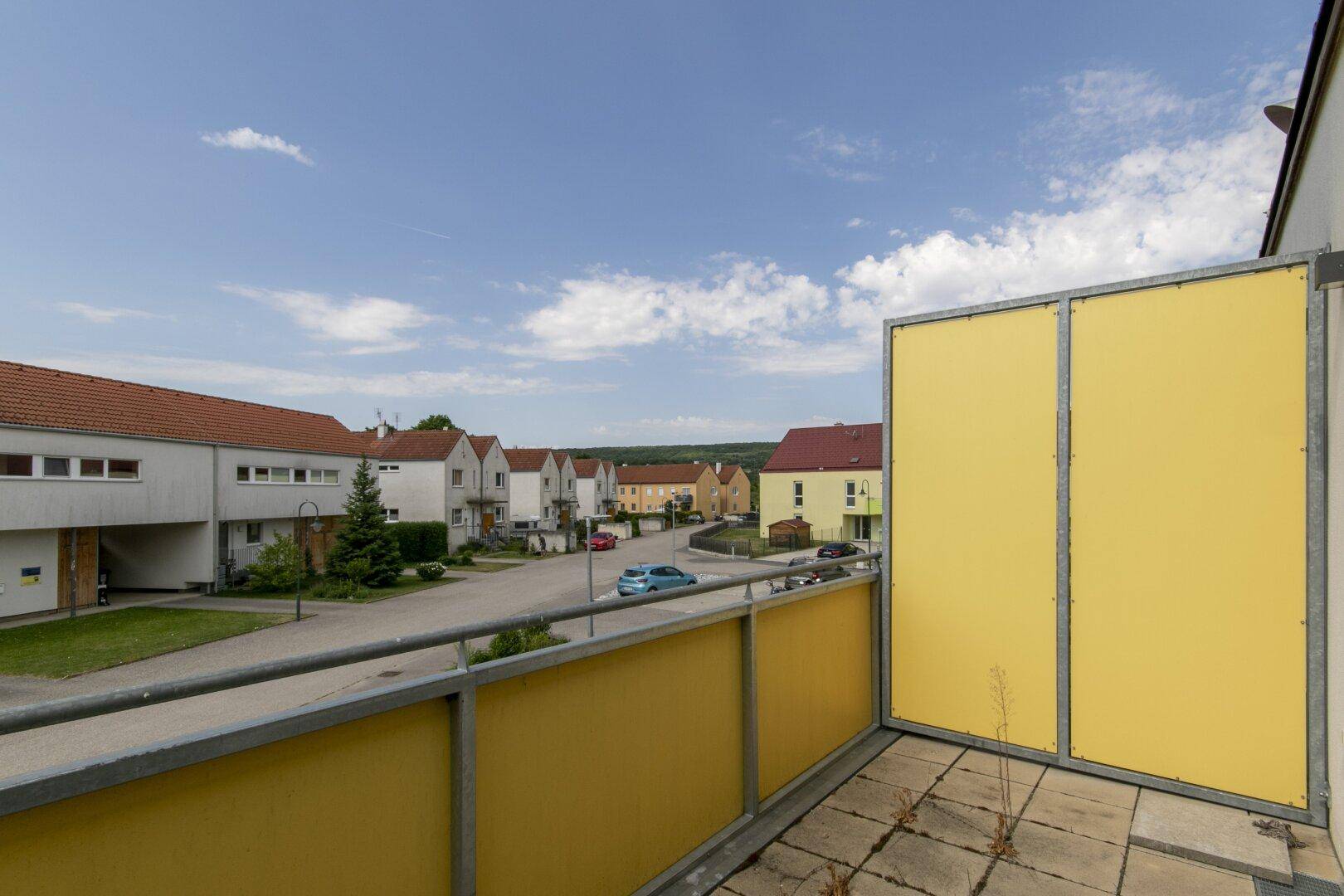 Heller Balkon mit seitlichem Blick auf die Wohnsiedlung und den blauen Himmel.