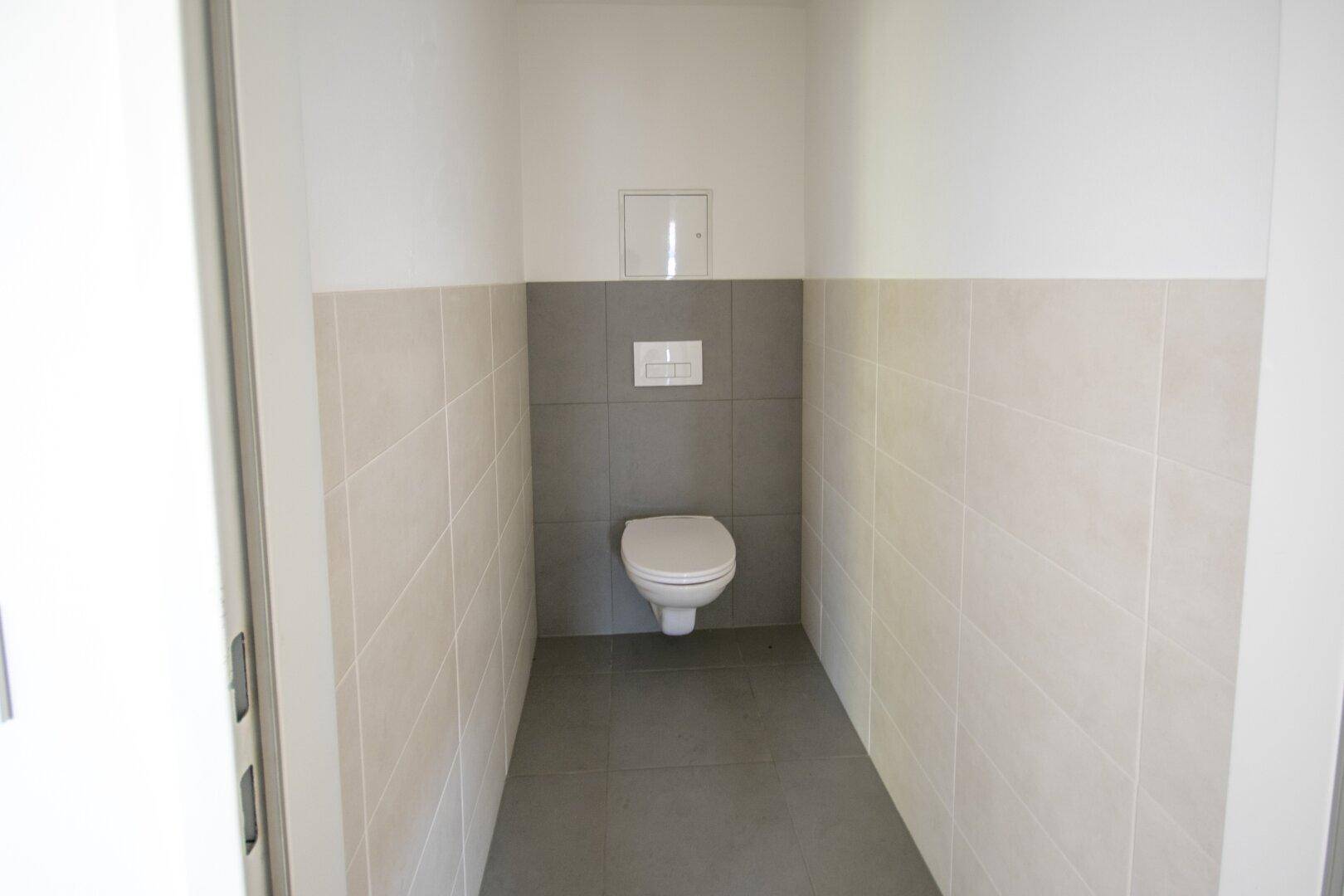 Modern gefliestes Gäste-WC mit wandhängendem WC und grauen Bodenfliesen.