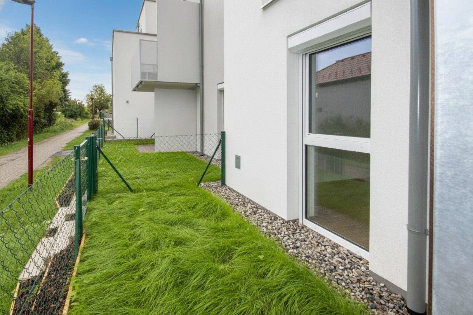 Seitenansicht eines Neubaus mit Fenster und kleiner Rasenfläche entlang der Fassade.
