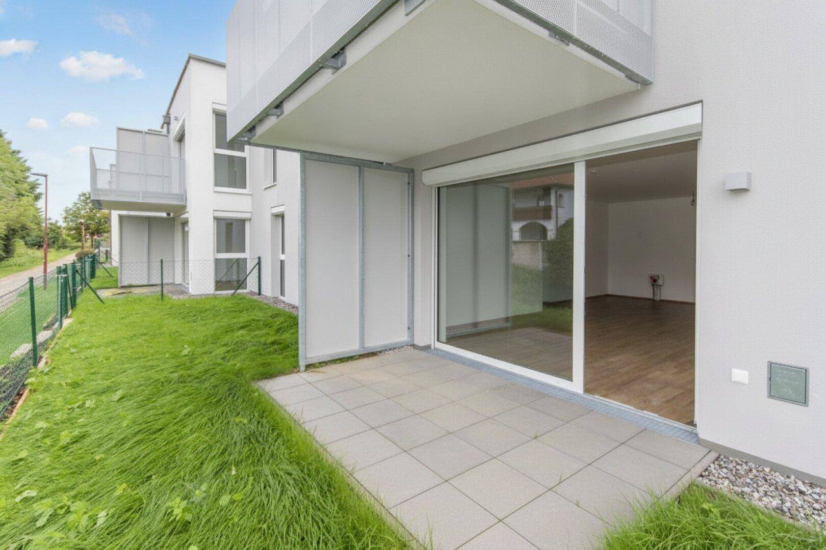 Gepflasterte Terrasse mit direktem Zugang zum Wohnbereich und Blick auf den kleinen Garten.