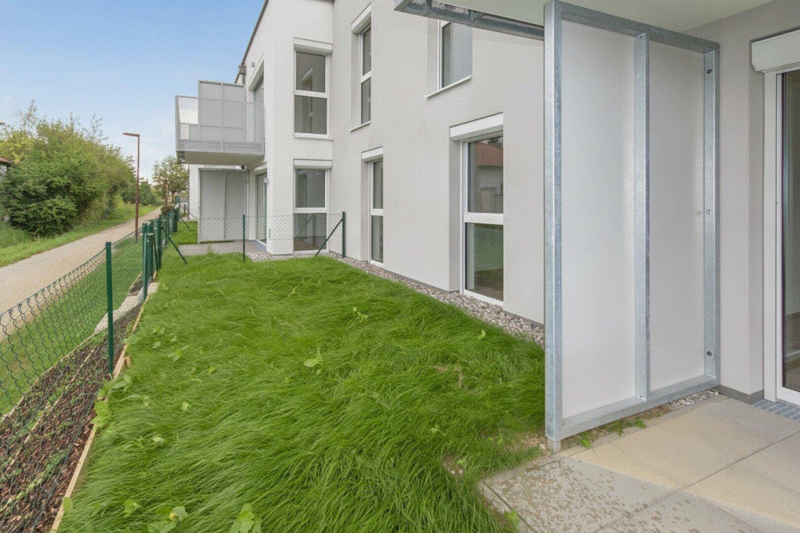 Außenansicht eines modernen Gebäudes mit kleinem Gartenbereich und Balkonen.