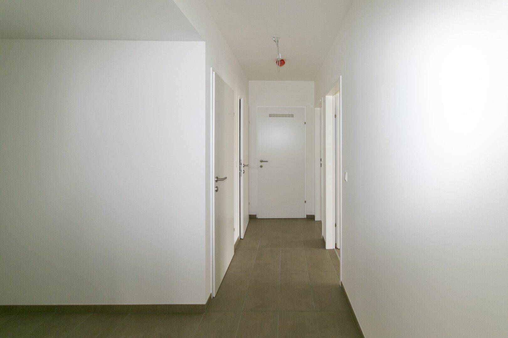 Langer, heller Flur mit Fliesenboden und mehreren Türen zu den angrenzenden Zimmern.