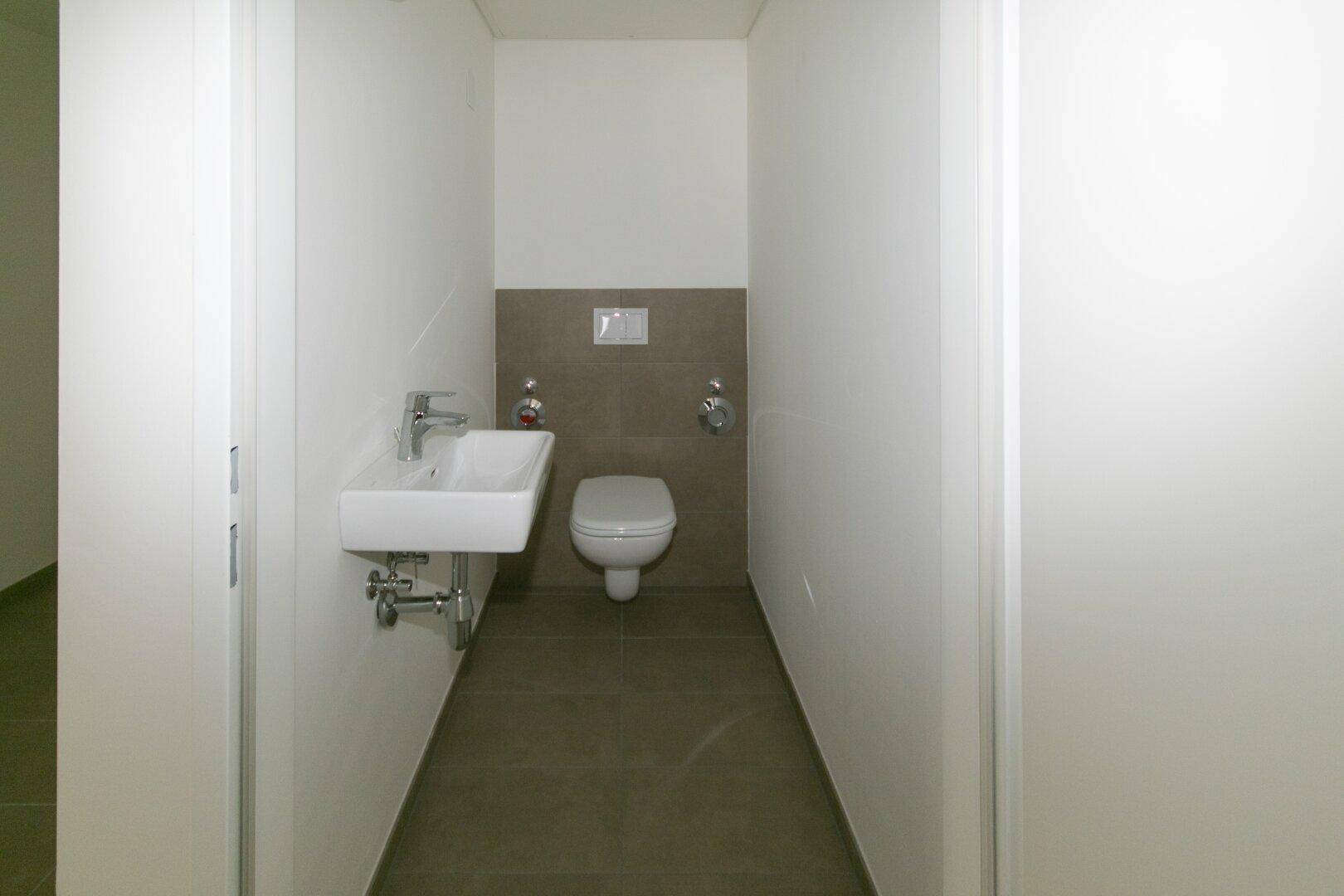 Funktionale Gästetoilette mit wandhängendem WC und kleinem Waschbecken, modern gefliest.