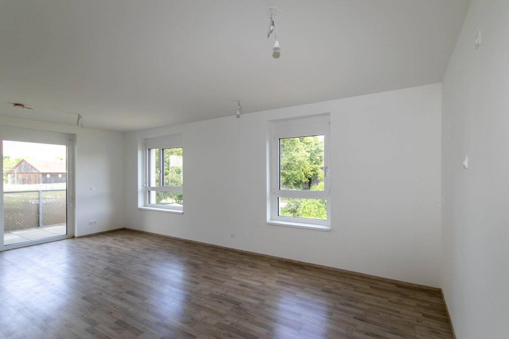 Helles Wohnzimmer mit großen Fenstern, Laminatboden und Blick ins Grüne.