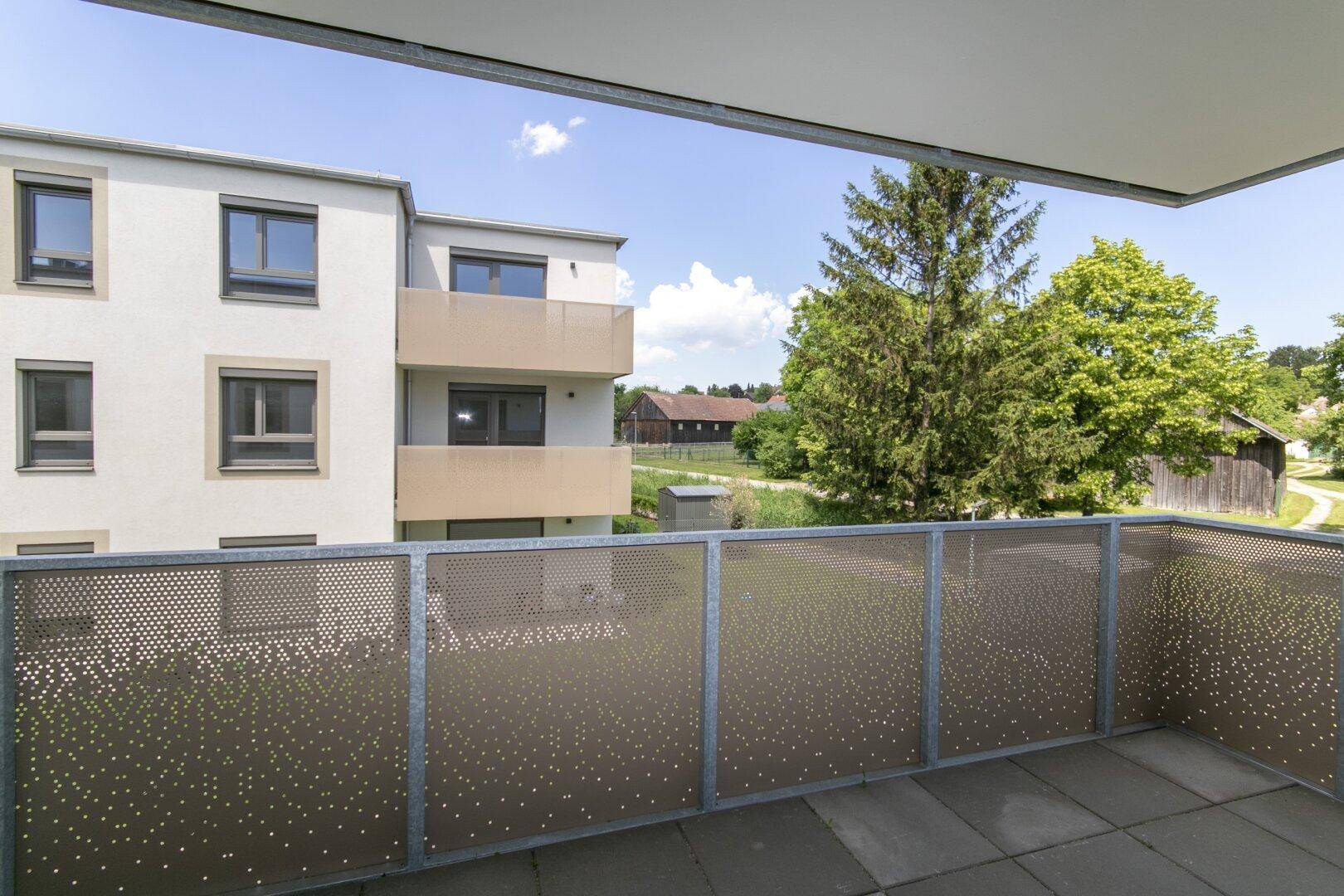 Heller Balkon mit perforiertem Metallgeländer und weitem Blick auf die Umgebung.