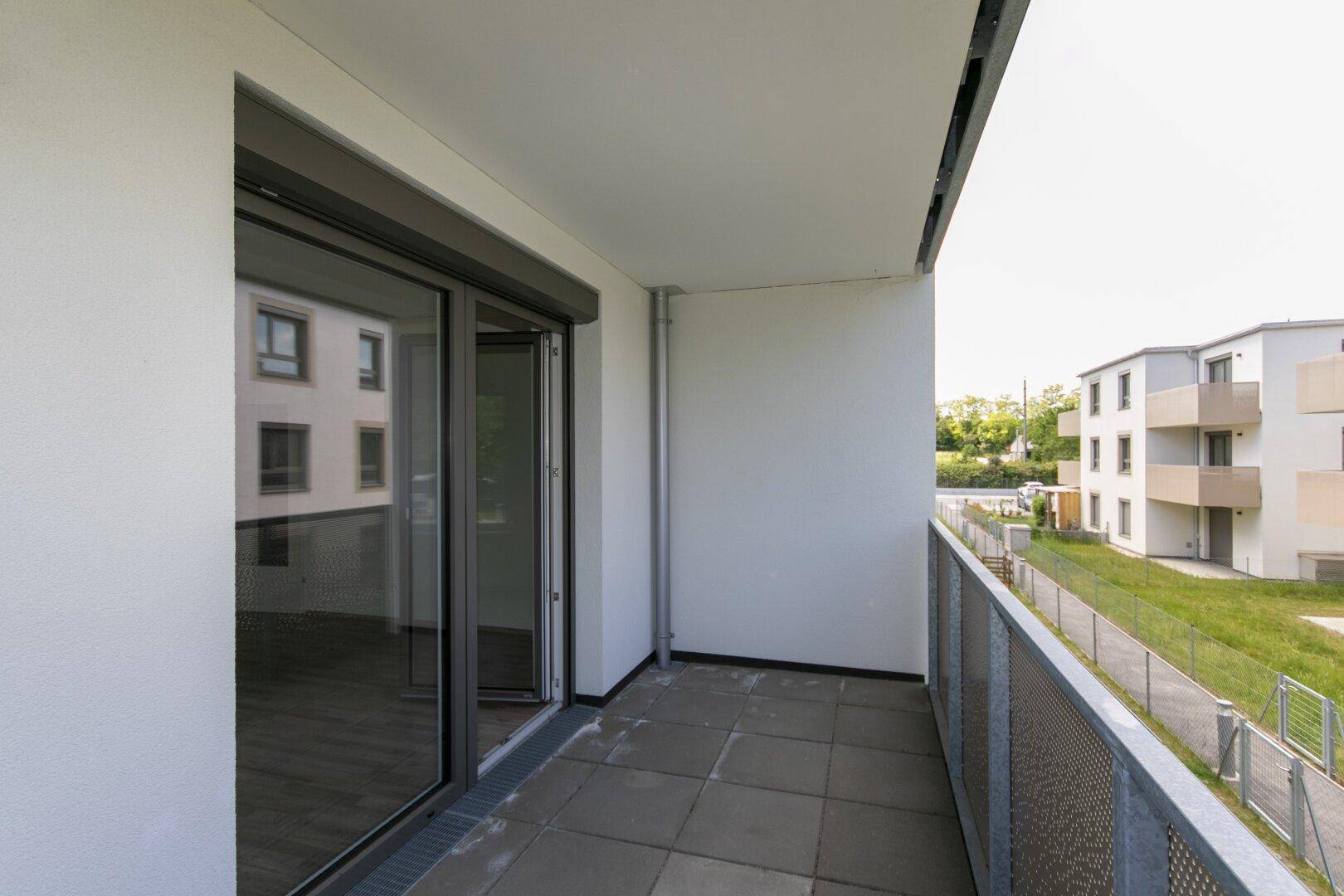 Leerer Balkon mit Fliesenboden und Blick auf die Fassade eines benachbarten Gebäudes.