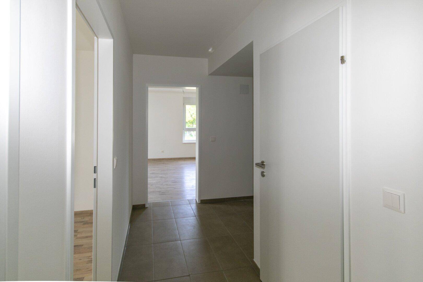 Flur mit Fliesenboden und Übergang zu einem Zimmer mit Laminatboden, hell und einladend.
