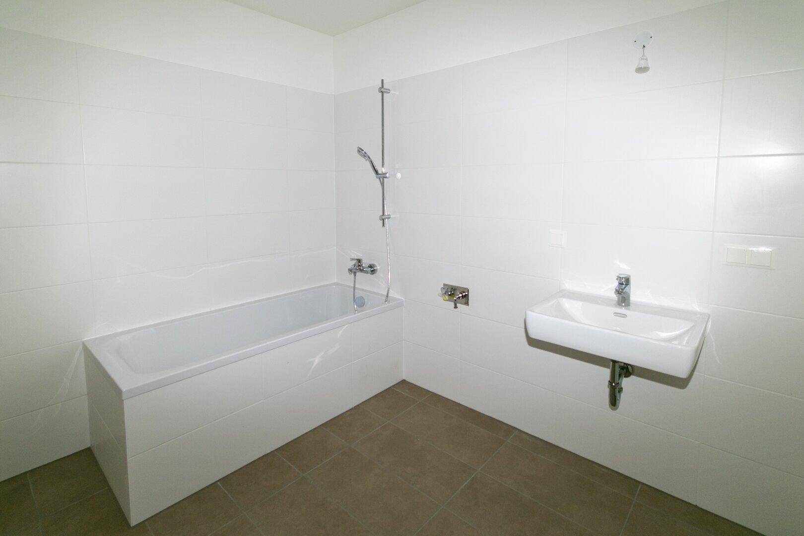 Funktionales Badezimmer mit Badewanne, Waschbecken und hellen Fliesen an Wänden und Boden.