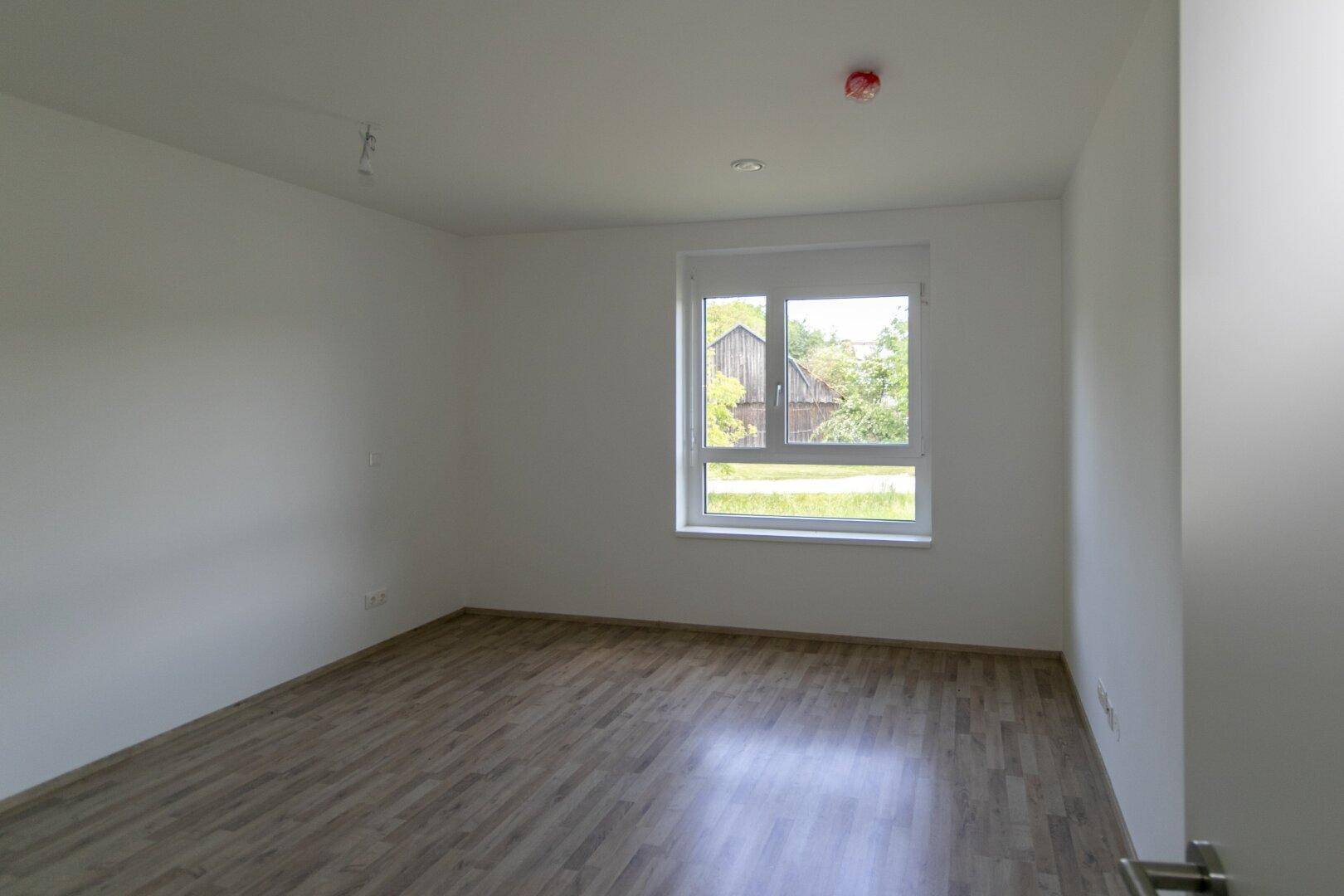Ruhiges Schlafzimmer mit Laminatboden und einem Fenster, das einen Blick ins Grüne bietet.